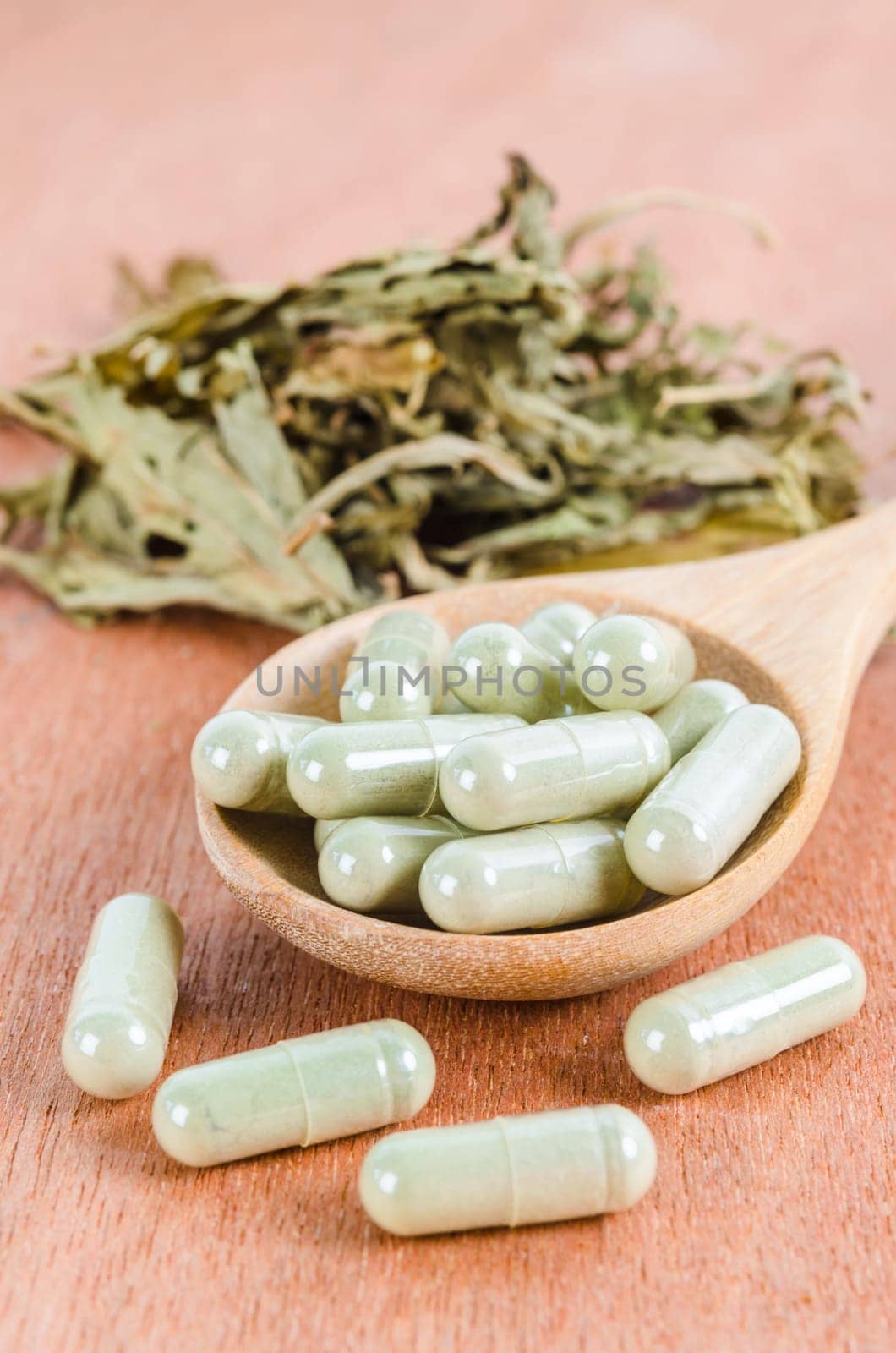 Pile of herbal medicine in capsules with herb dry leaf on wooden background.