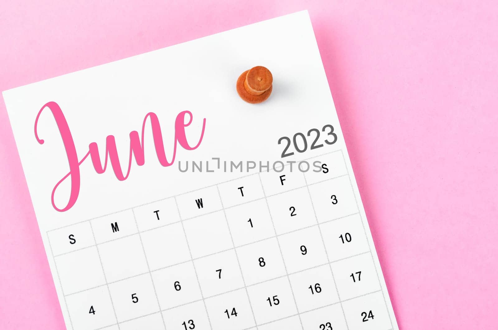 June 2023 calendar and wooden push pin on pink colour background.