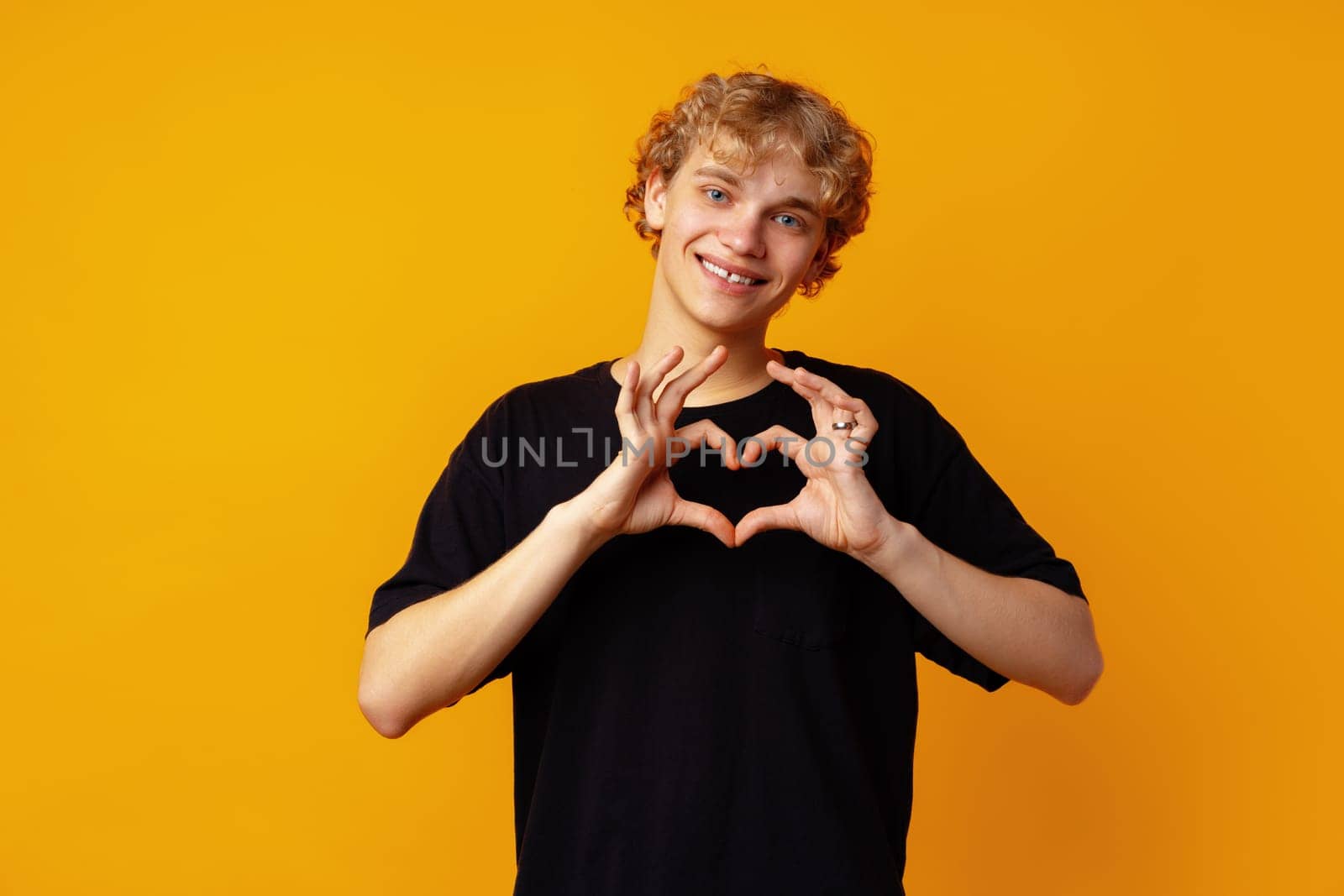 Young man on yellow background smiling and showing a heart shape with hands close up