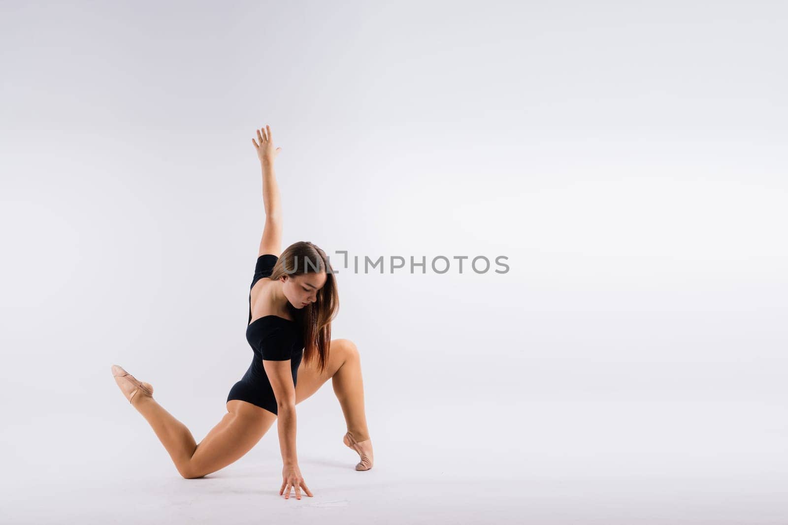 Flexible girl, rhythmic gymnastic artist jumping on white dark background. Grace in motion, action.