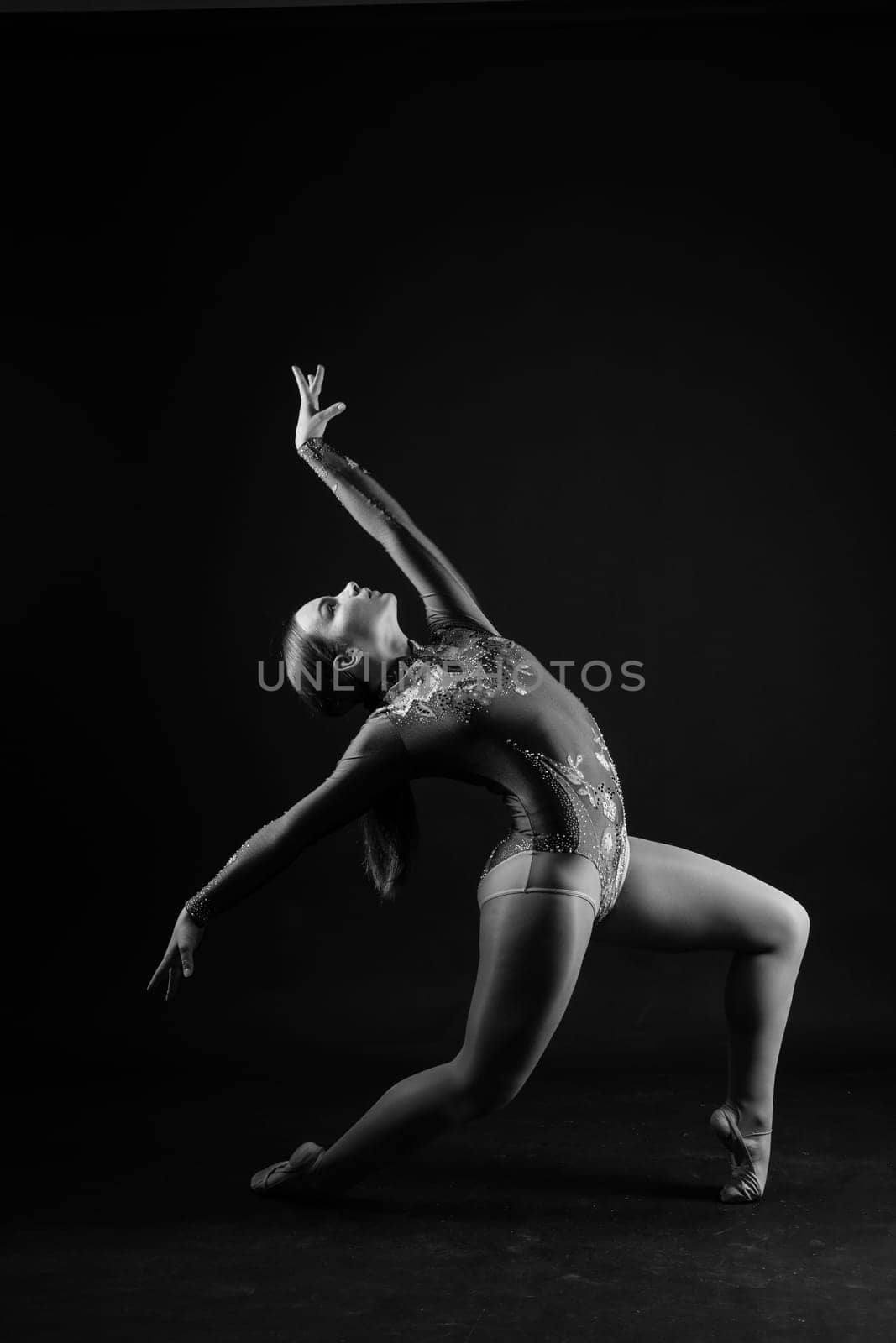 Flexible girl, rhythmic gymnastics artist jumping on white dark background. Grace in motion, action. by Zelenin