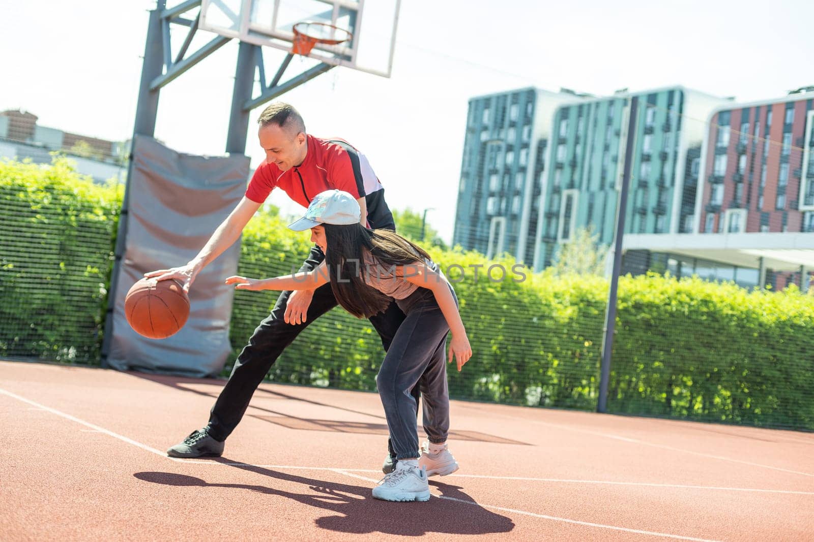 Happy father and teen daughter embracing and looking at camera outside at basketball court