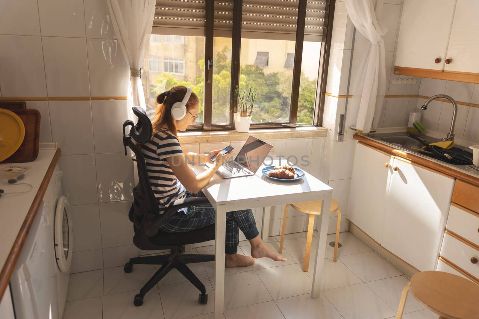 An adult business woman in headphones working at the kitchen table. Mid shot