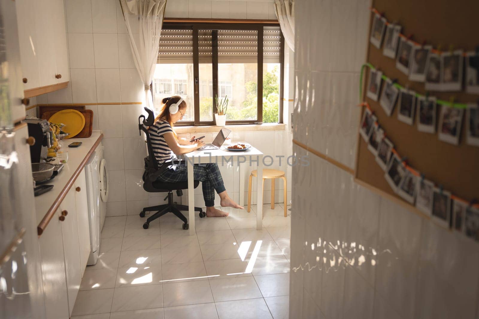 An adult business woman in headphones working at the kitchen. Mid shot