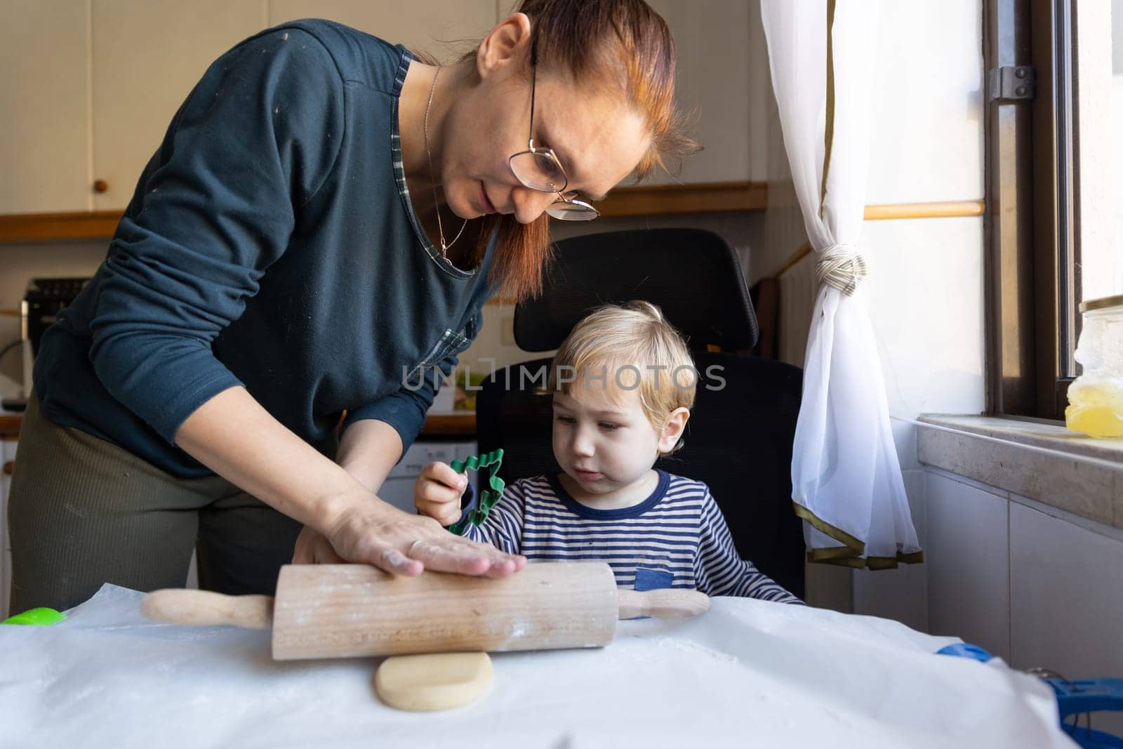 Family cooking - a woman rolling out the dough and her little son looking at her hands. Mid shot