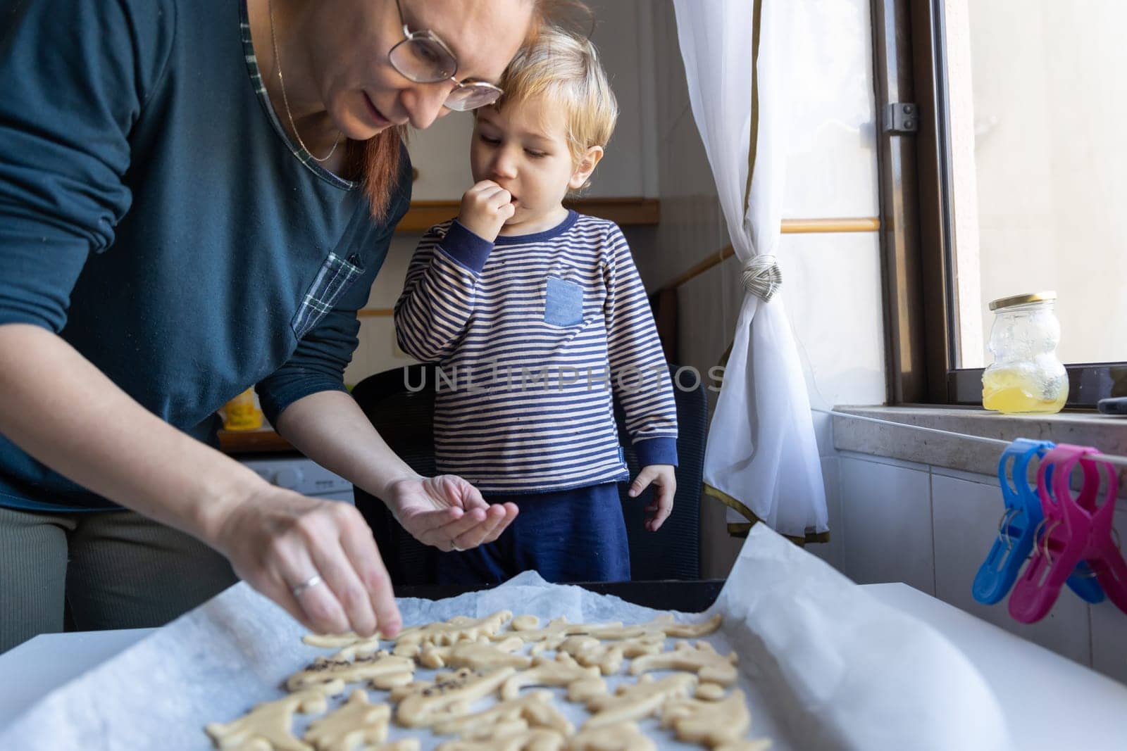 Family making cookies - a woman with her little son sprinkle sugar on the dough by Studia72