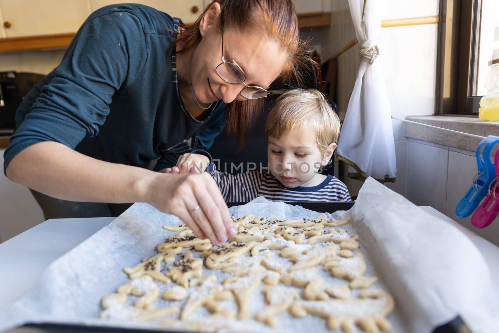 Family making cookies - a woman with her little son make cookies in the shape of dinosaurs by Studia72