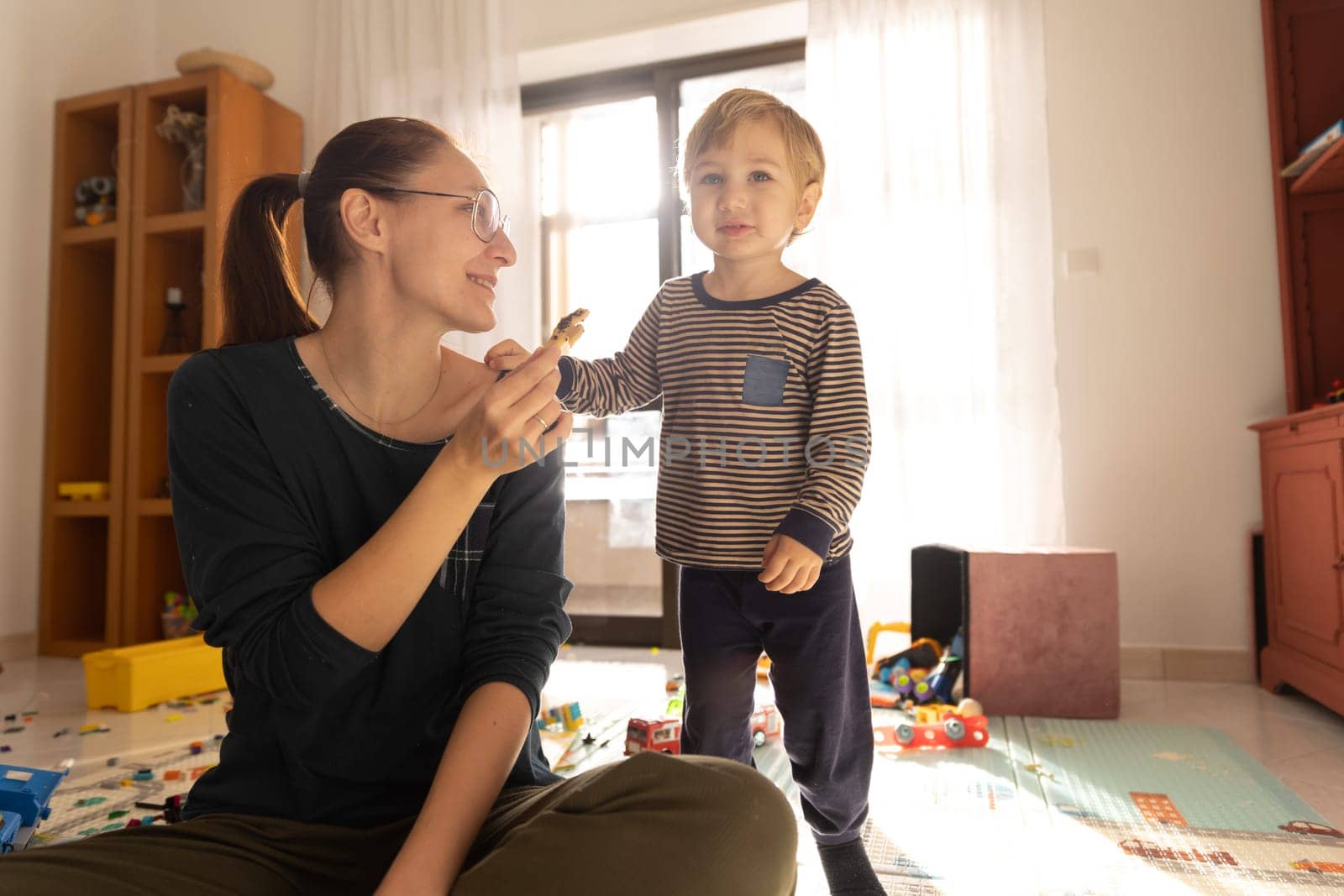 Mother and son in the playroom - a woman holds a cookie and a boy looks ahead. Mid shot