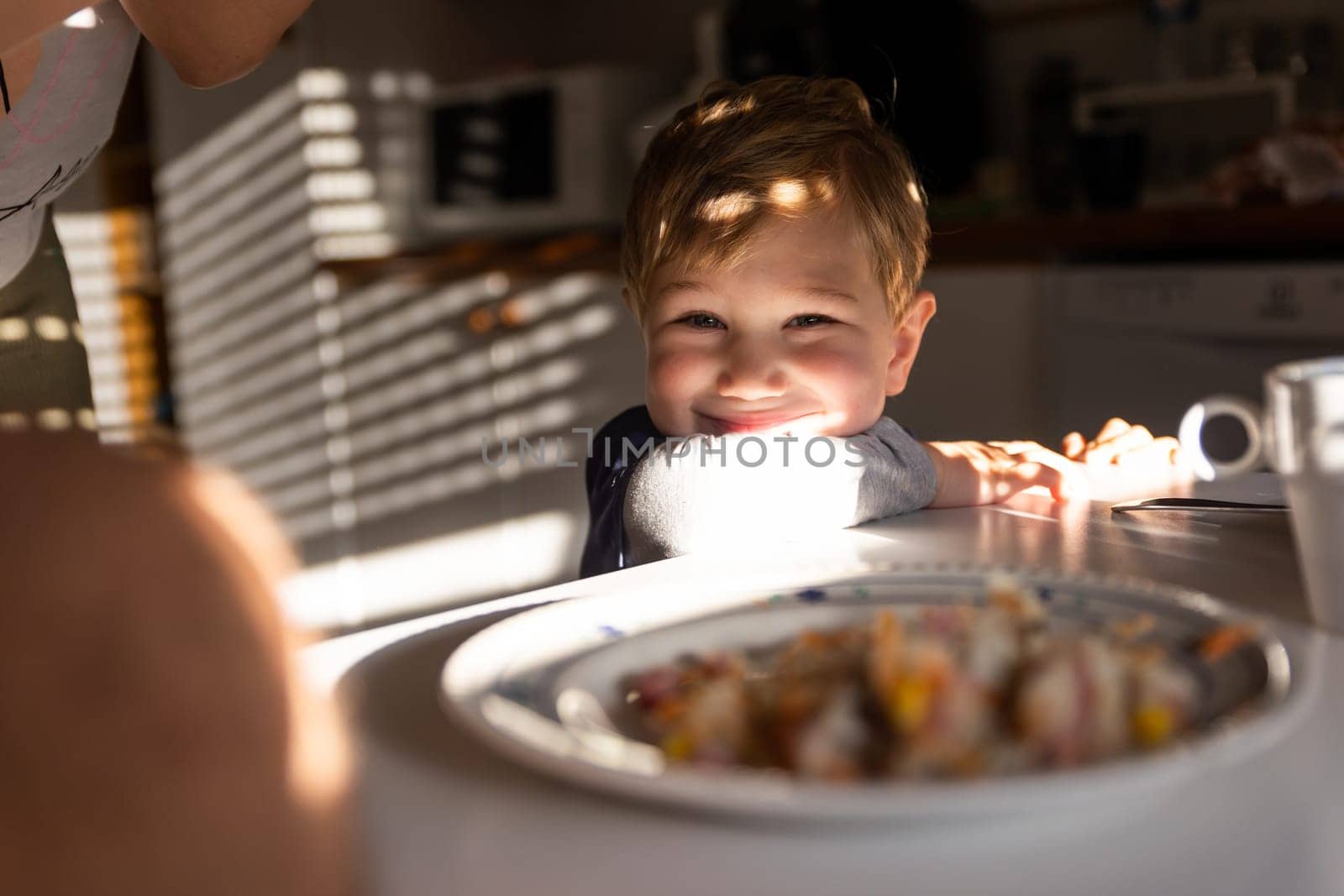 Little smiling boy sitting at the kitchen table. Mid shot