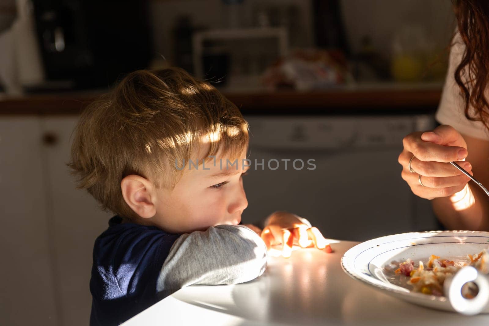 A little boy sits at the kitchen table with his mom by Studia72