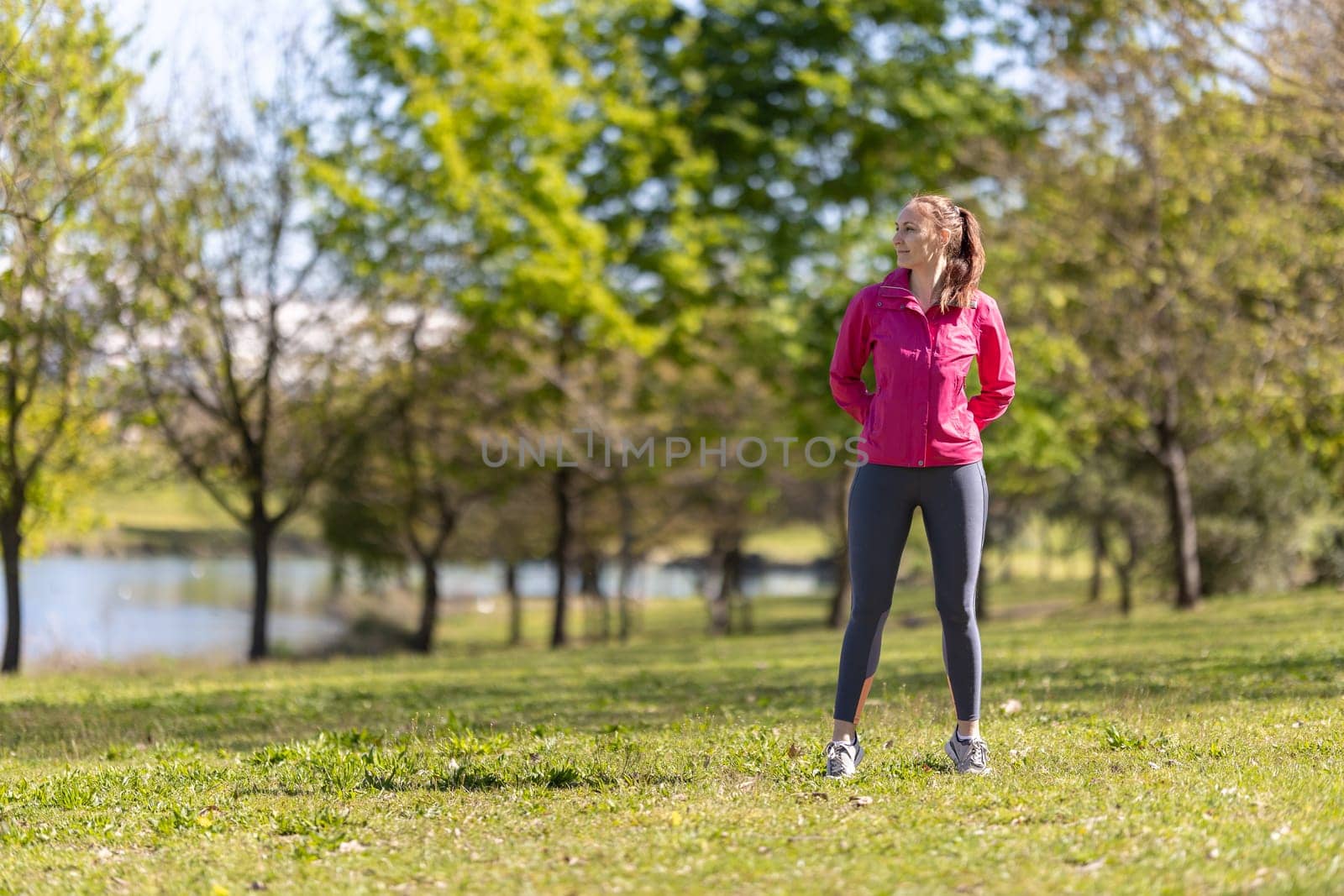An adult smiling woman in sports clothes standing on the field and looking to the side. Mid shot