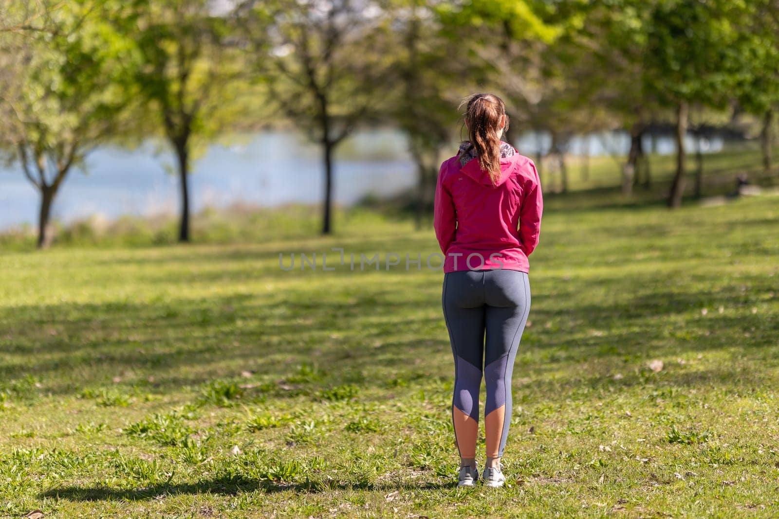 An adult woman in sports clothes standing on the field - view from the back. Mid shot