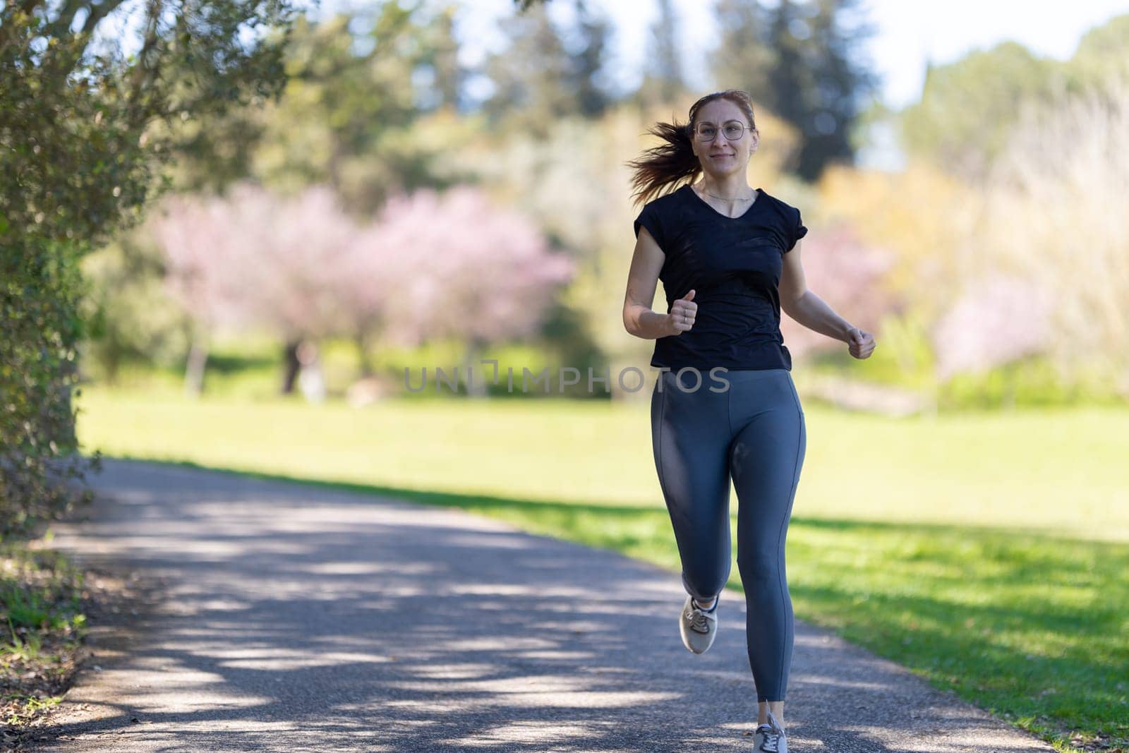 An adult smiling woman jogging on nature. Mid shot