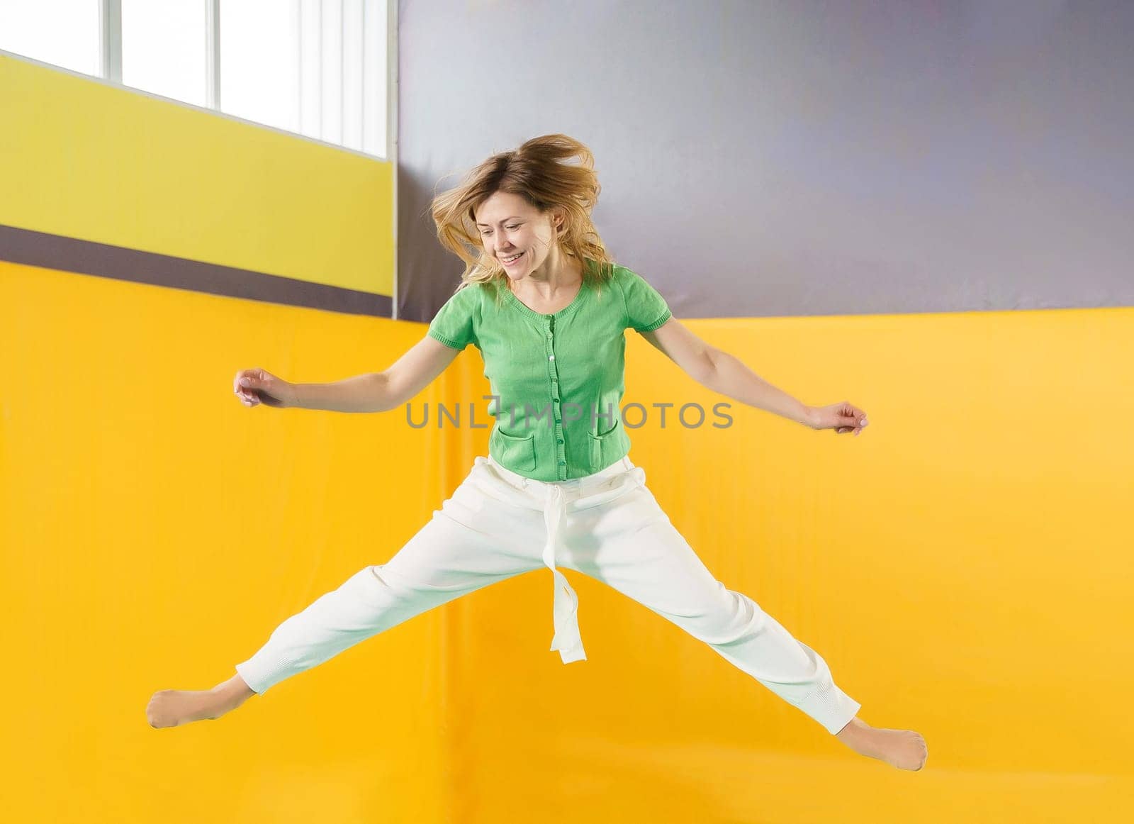 Young woman jumping and bouncing on a trampoline in sport center by Mariakray