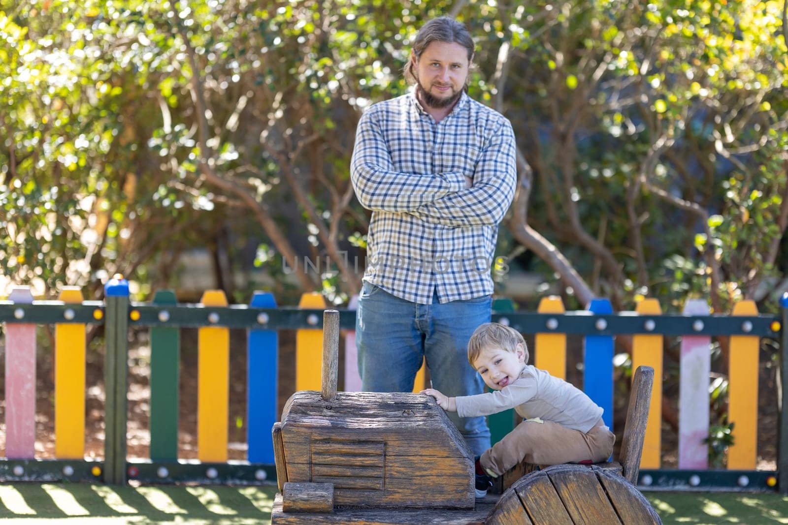 Father with his hands crossed and his little son on the playground. Mid shot