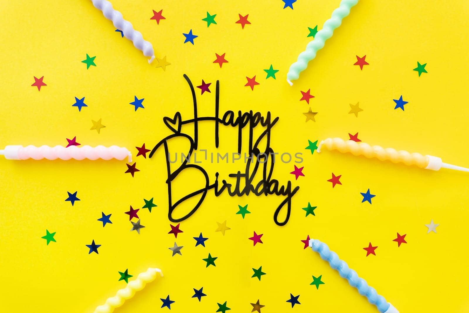 The inscription happy birthday on a yellow background. Festive background with candles, confetti in the form of stars with copy space
