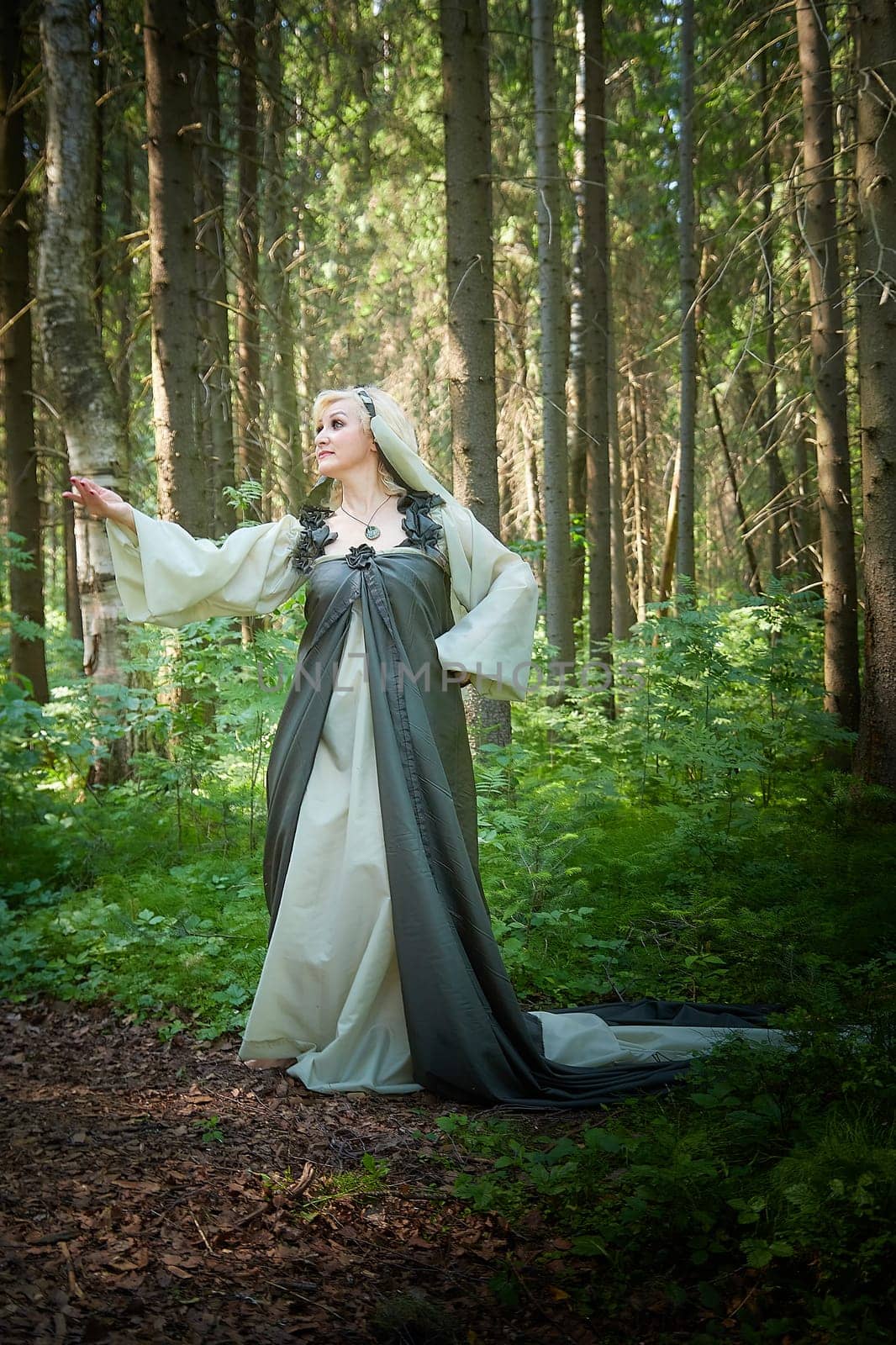 Adult mature woman 40-60 in a green long fairy dress in forest. Photo shoot in style of dryad and queen of nature. Fairy in beautiful green summer forest. Concept of caring for nature