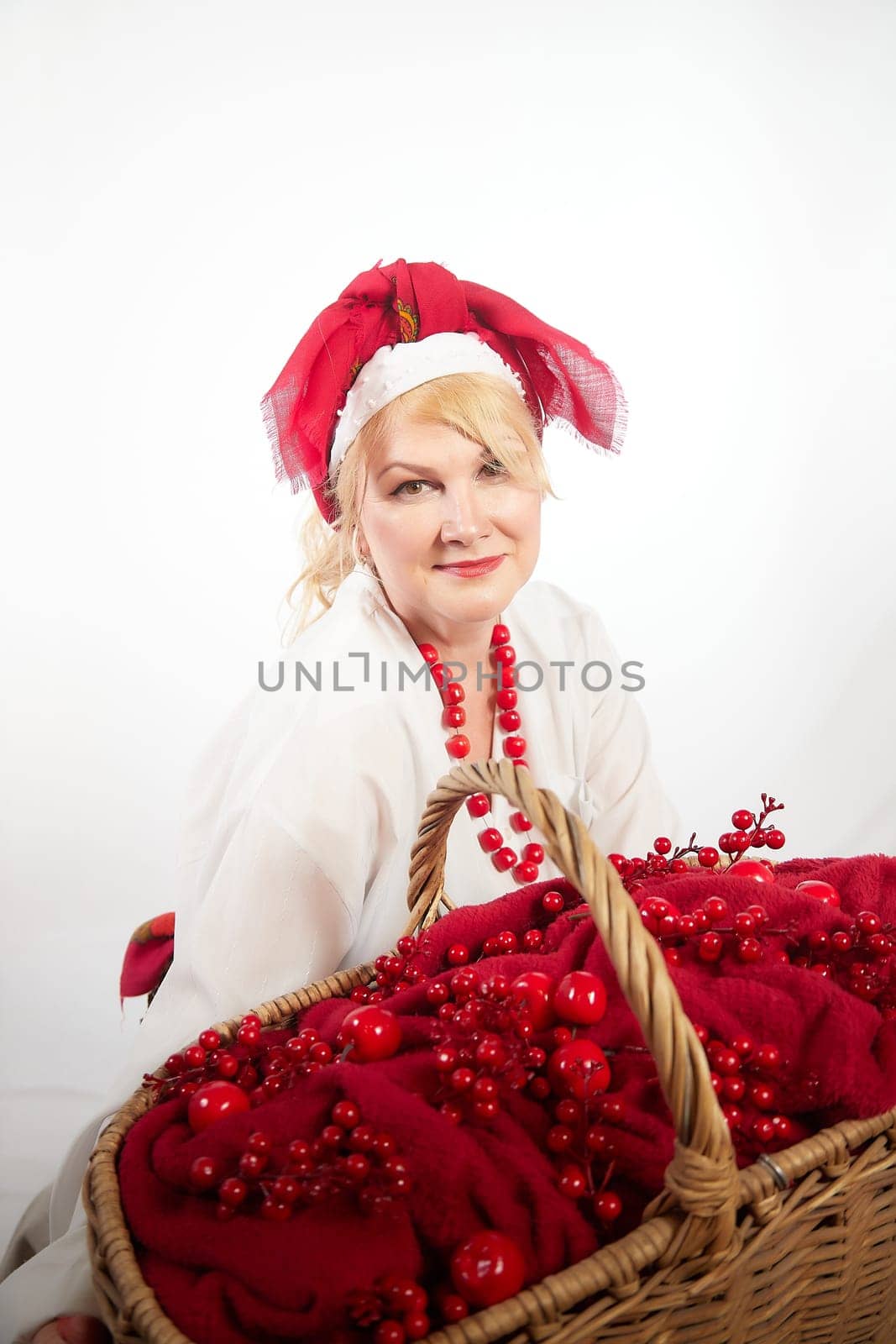 Cheerful funny adult mature woman solokha in a red knitted shawl. Female model in clothes of national ethnic Slavic style. Stylized Ukrainian, Belarusian or Russian woman poses in a comic photo shoot by keleny