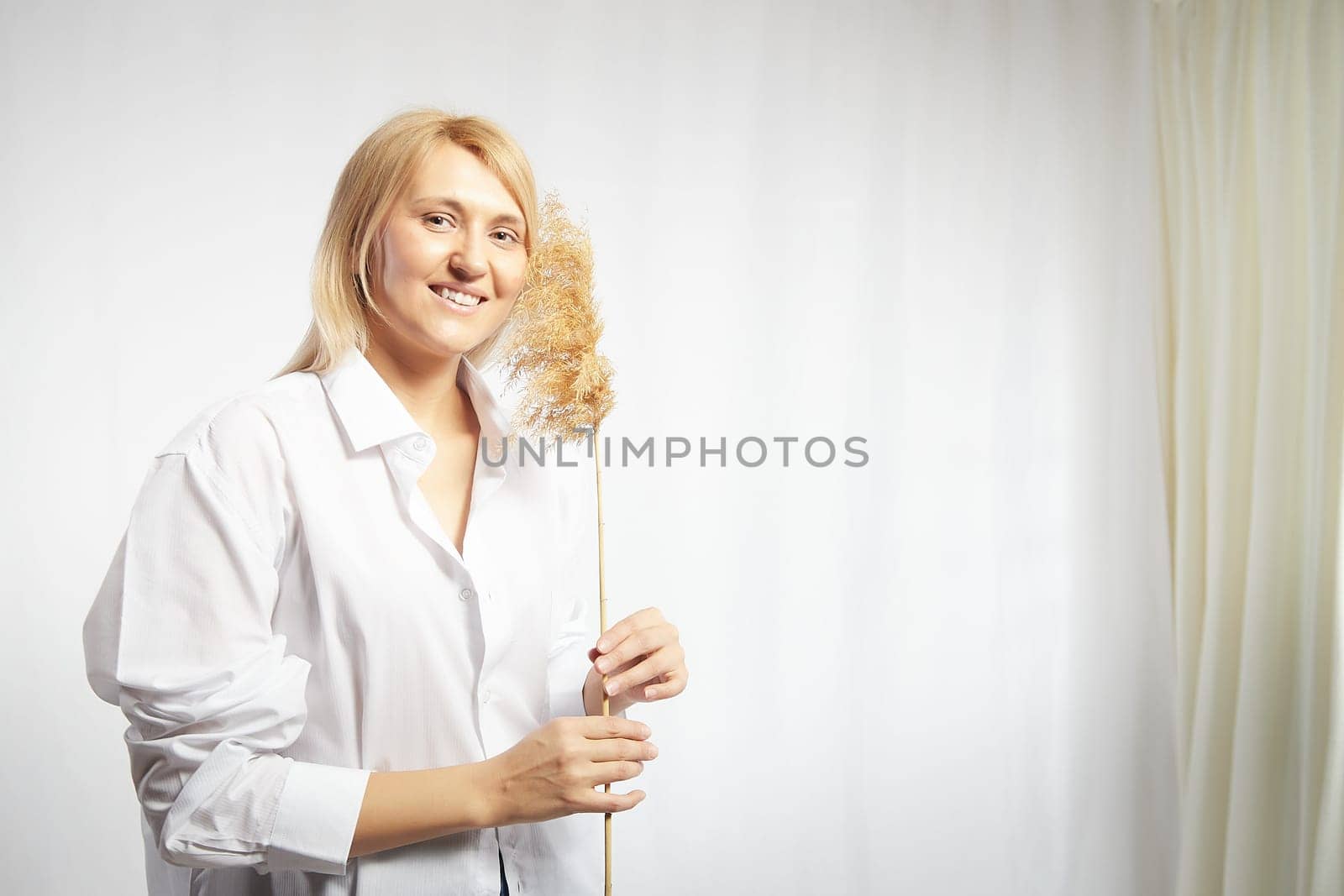 Portrait of a pretty blonde smiling woman with a soft ear in hands posing on a white background. Happy girl model in white shirt in studio. The concept of softness, tenderness and dreams. Copy space by keleny