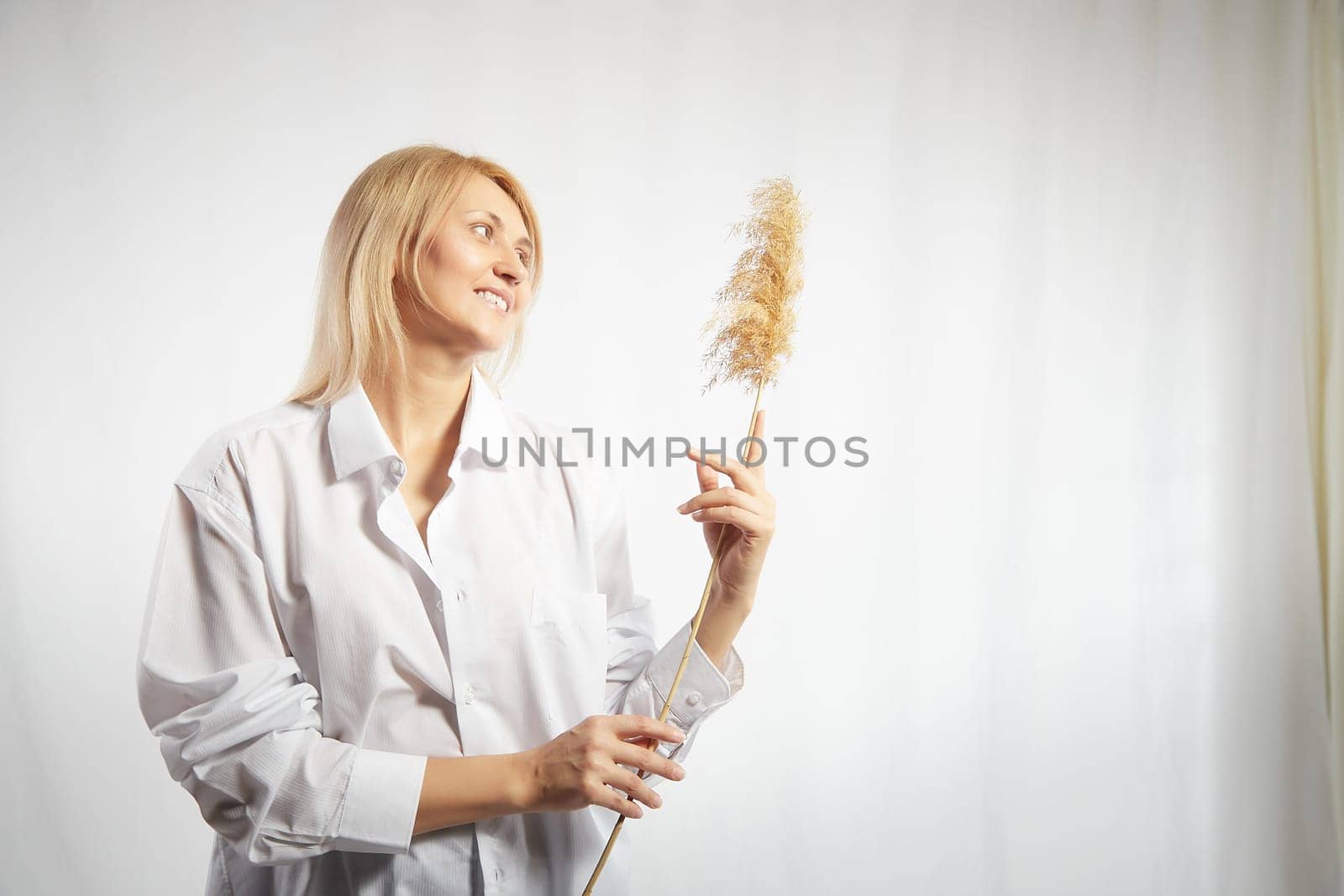 Portrait of a pretty blonde smiling woman with a soft ear in hands posing on a white background. Happy girl model in white shirt in studio. The concept of softness, tenderness and dreams. Copy space by keleny