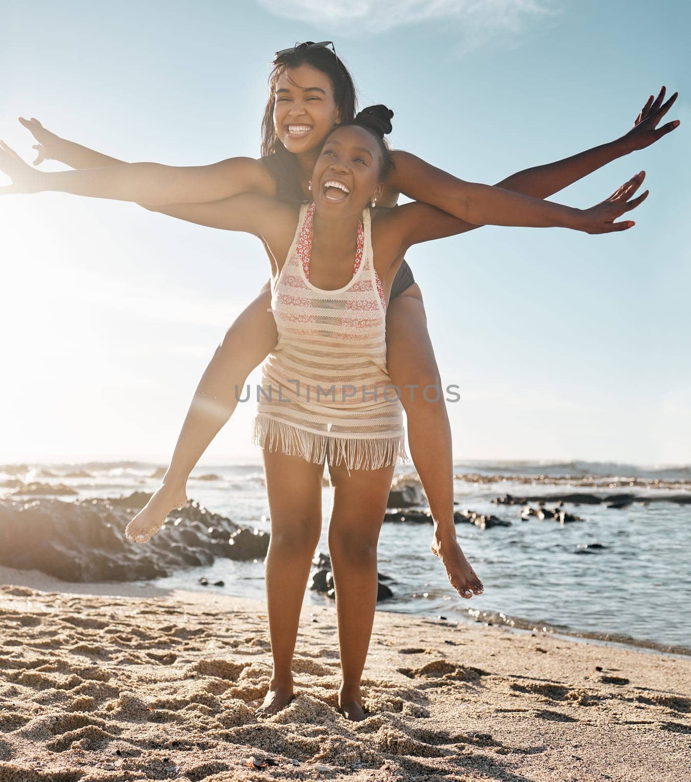 Friends, laughing or piggyback airplane by beach, ocean or sea in social gathering, vacation comedy or summer holiday. Smile, happy or black woman carrying girl in travel fun, bonding or comic games by YuriArcurs