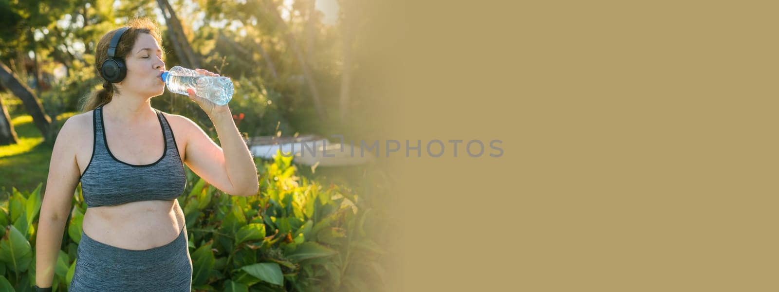 Overweight woman drinking water after jogging in the park. Portrait of young plus-size thirsty woman with a bottle of water outdoors. Sports, healthcare, weight loosing, fitness, well-being concept