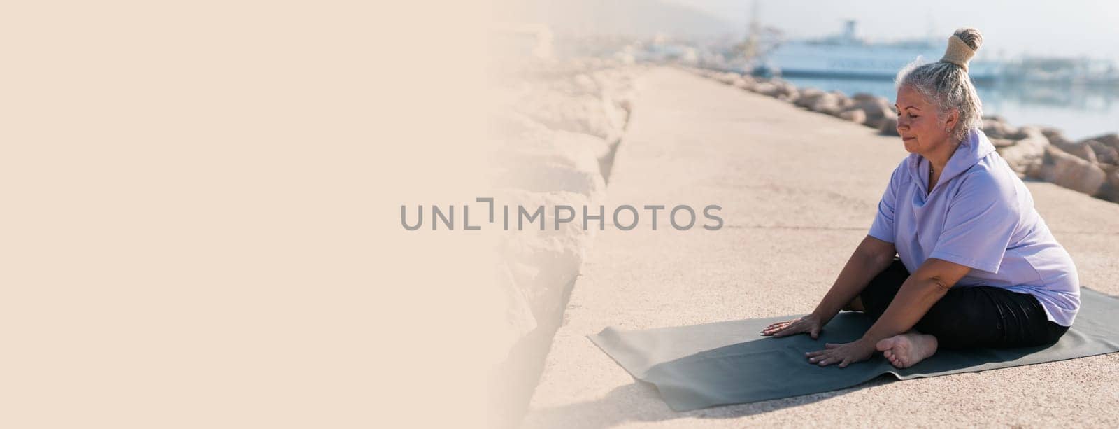 Banner Senior woman with dreadlocks in stretching position by the sea at morning copy space. Elderly woman doing yoga near beach. by Satura86