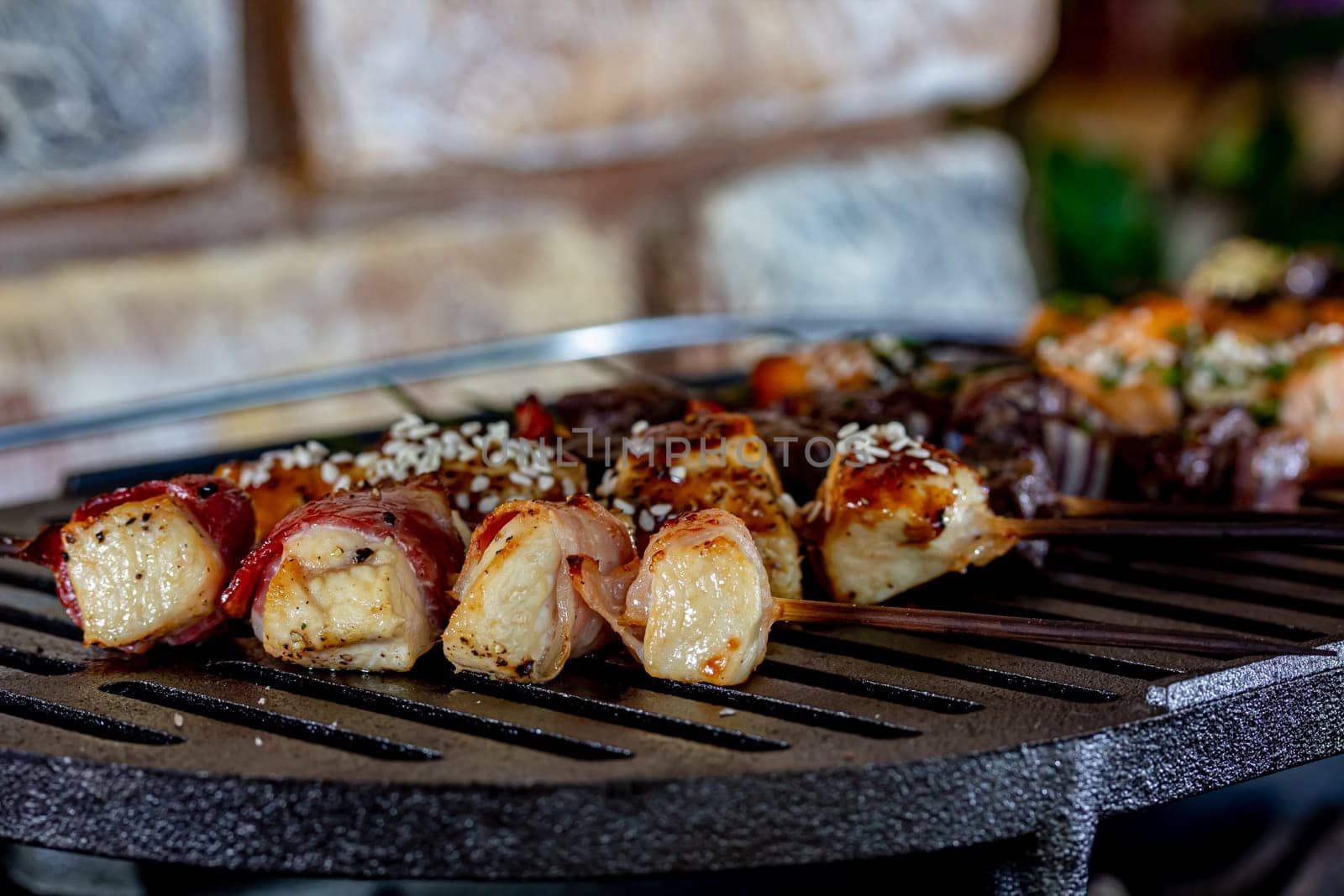 A lot of mini-kebabs of meat, fish, chicken, shrimp, vegetables on wooden skewers are fried on a small cast-iron grill.