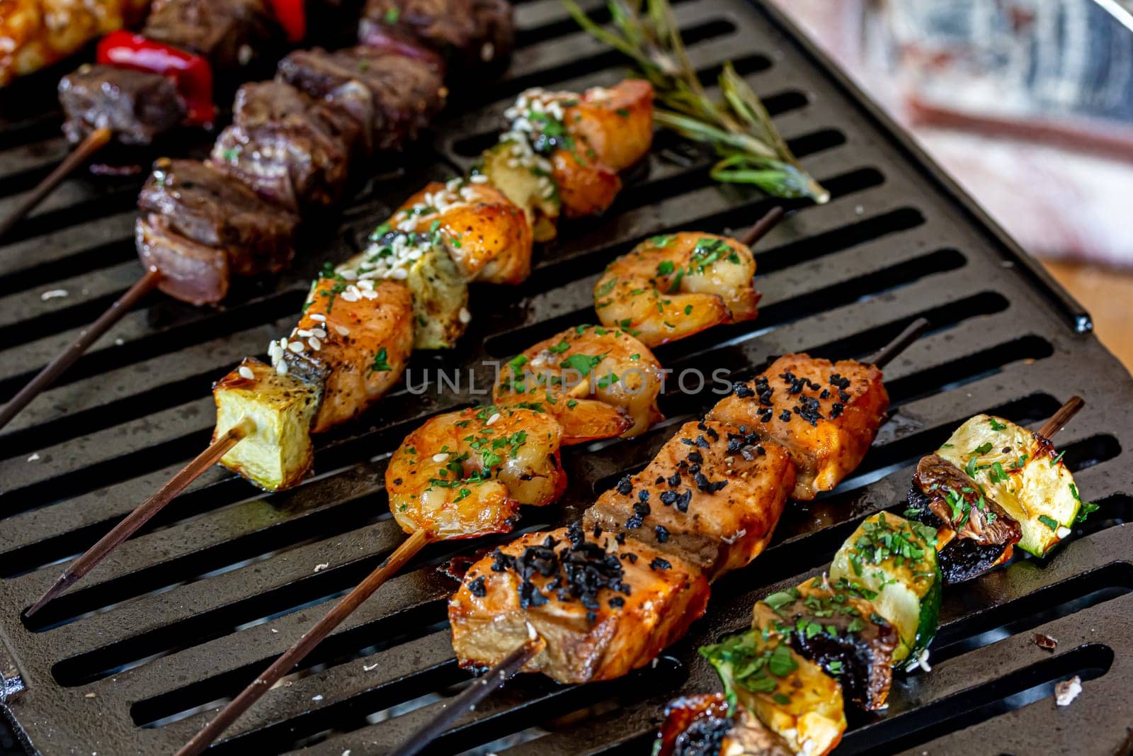 A lot of mini-kebabs of meat, fish, chicken, shrimp, vegetables on wooden skewers are fried on a small cast-iron grill by Milanchikov