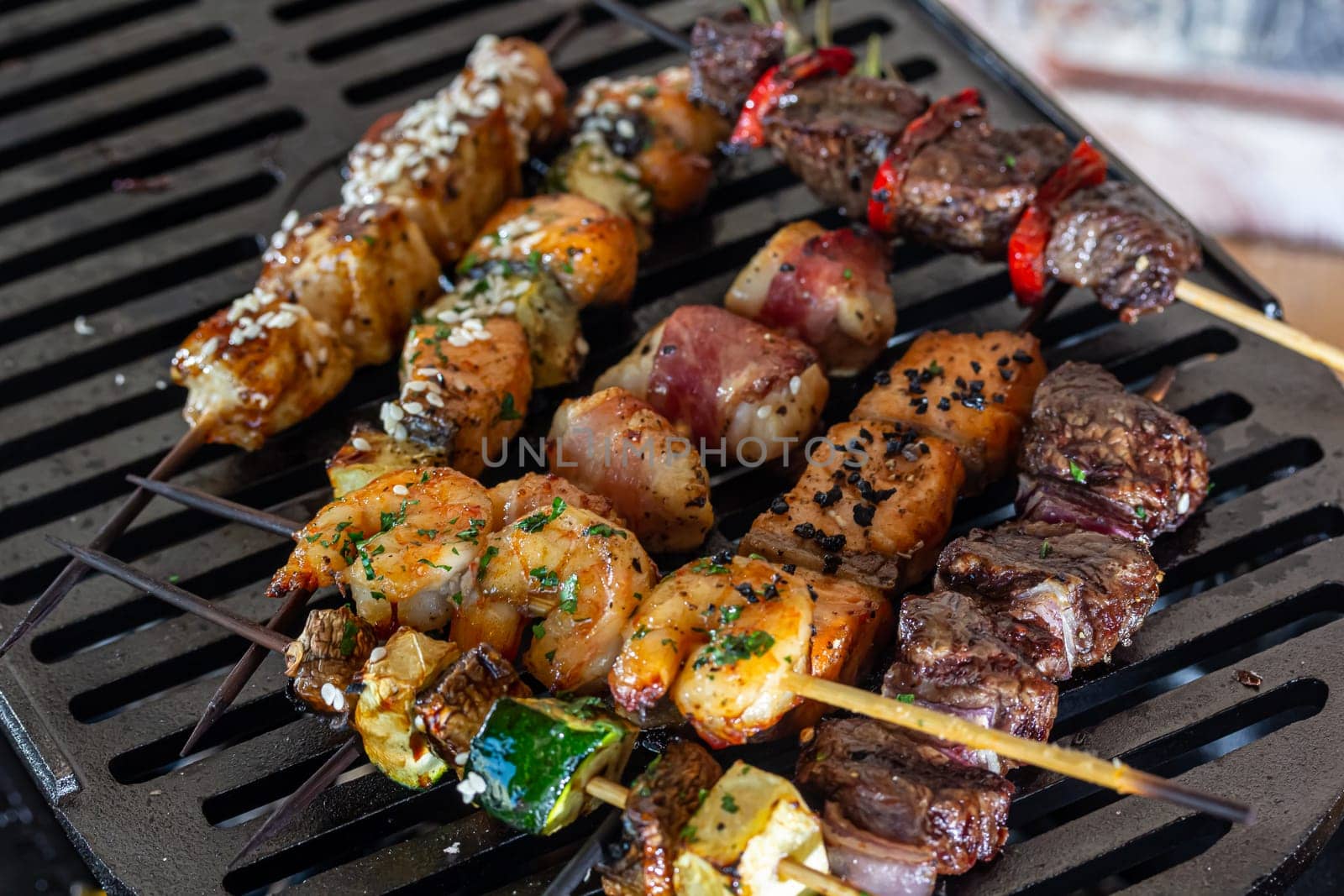 A lot of mini-kebabs of meat, fish, chicken, shrimp, vegetables on wooden skewers are fried on a small cast-iron grill by Milanchikov