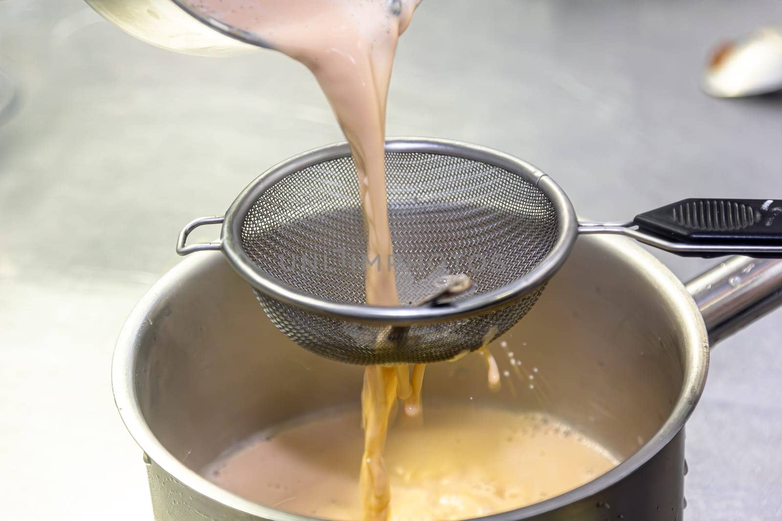 Cooking in the restaurant kitchen. Sifting sauce through a sieve. Chef is filtering sauce. High quality photo by Milanchikov