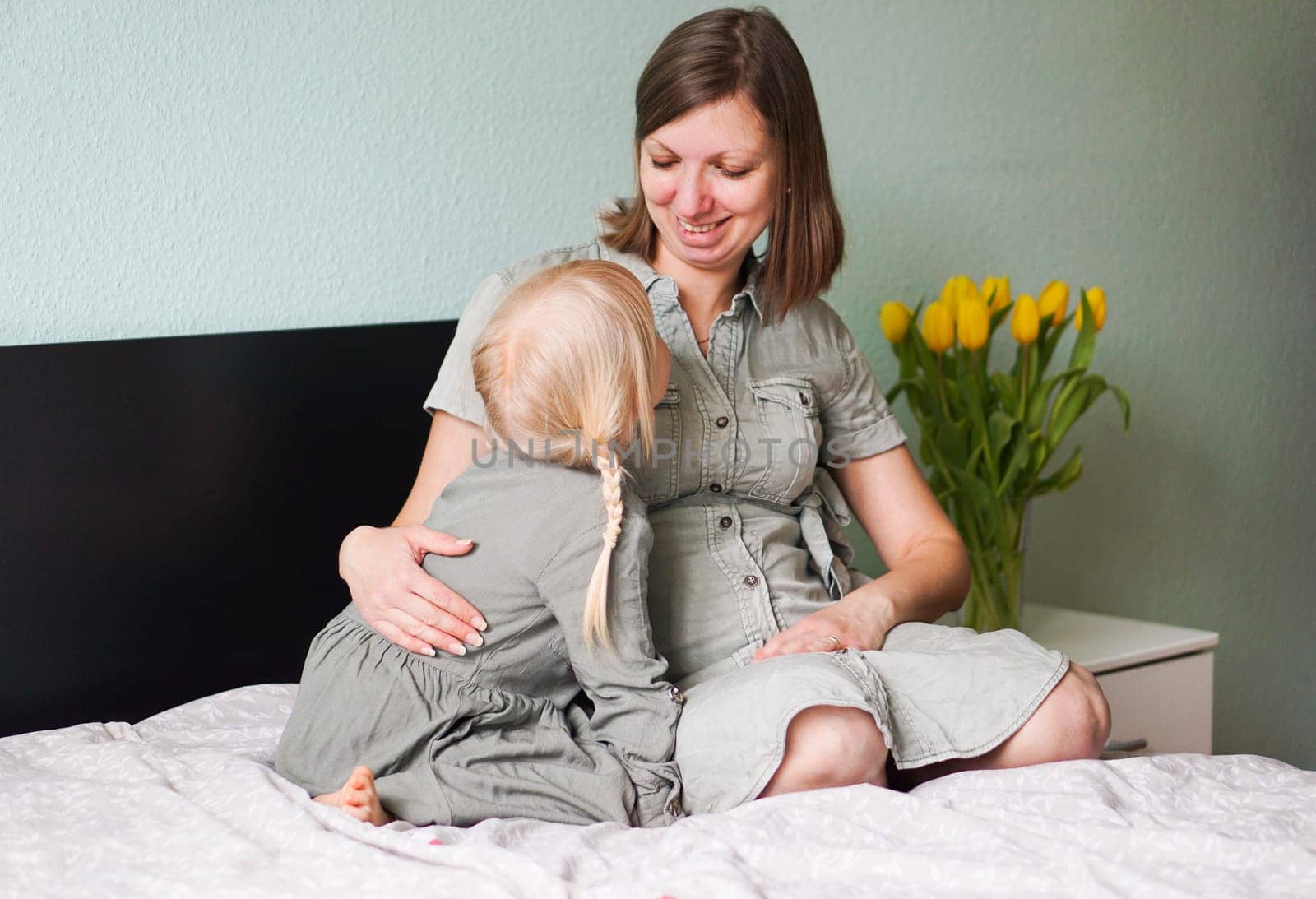 Smiling pregnant woman with her little daughter are talking and spending time together at home. by tanjas_photoarts