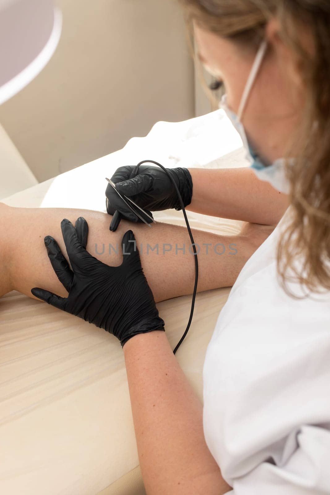 Dermatologist Doing Hair Removal Electrolysis Procedure On Woman's Leg, Shin. Electric Epilation In Beauty Salon. Vertical Plane. Authentic High quality photo