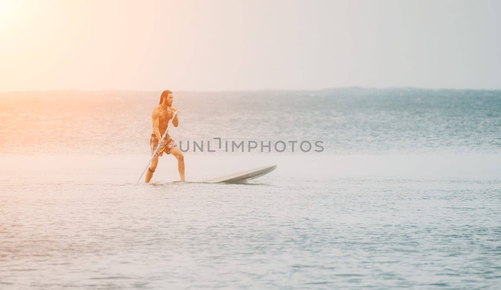 Sea man sup. Asian athlete man swimming in sea and paddleboarding at summer sunset. Healthy strong male enjoy outdoor active lifestyle and water sports on holiday vacation. by panophotograph