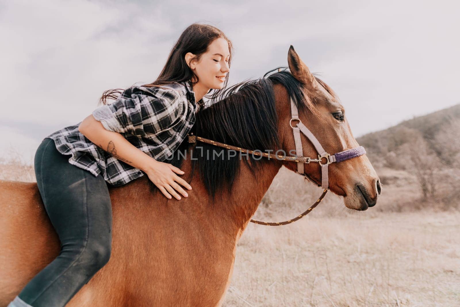 Young happy woman in hat with her horse in evening sunset light. Outdoor photography with fashion model girl. Lifestyle mood. Concept of outdoor riding, sports and recreation. by panophotograph
