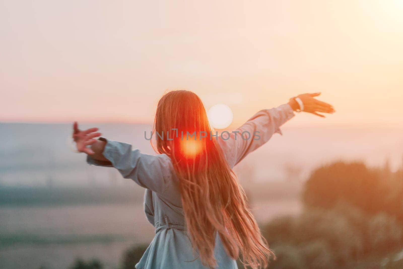 Happy woman standing with her back on the sunset in nature in summer with open hands. Romantic beautiful bride in white boho dress posing with mountains on sunset by panophotograph