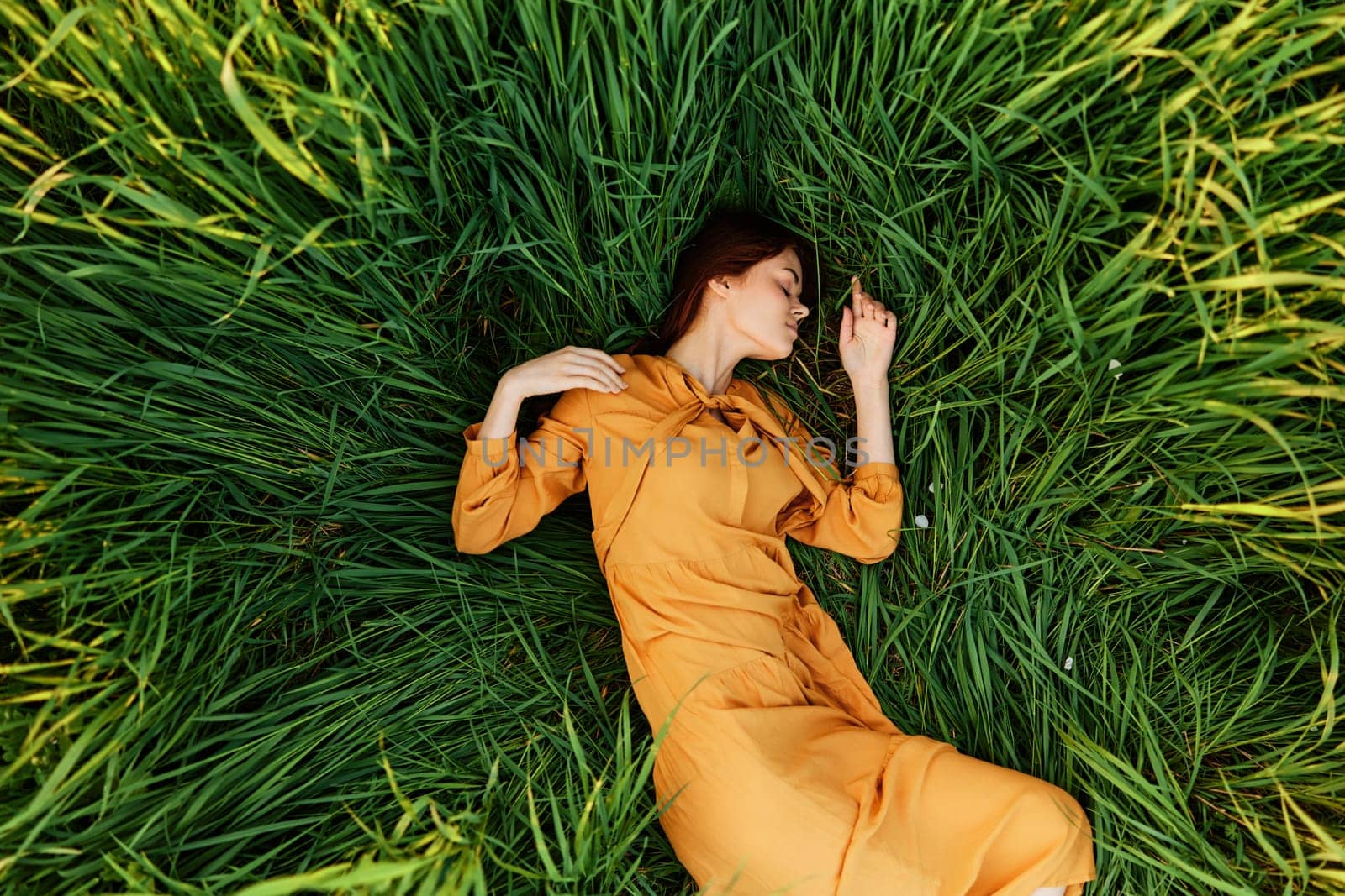 a relaxed woman enjoys summer lying in the tall green grass with her eyes closed. Photo taken from above by Vichizh