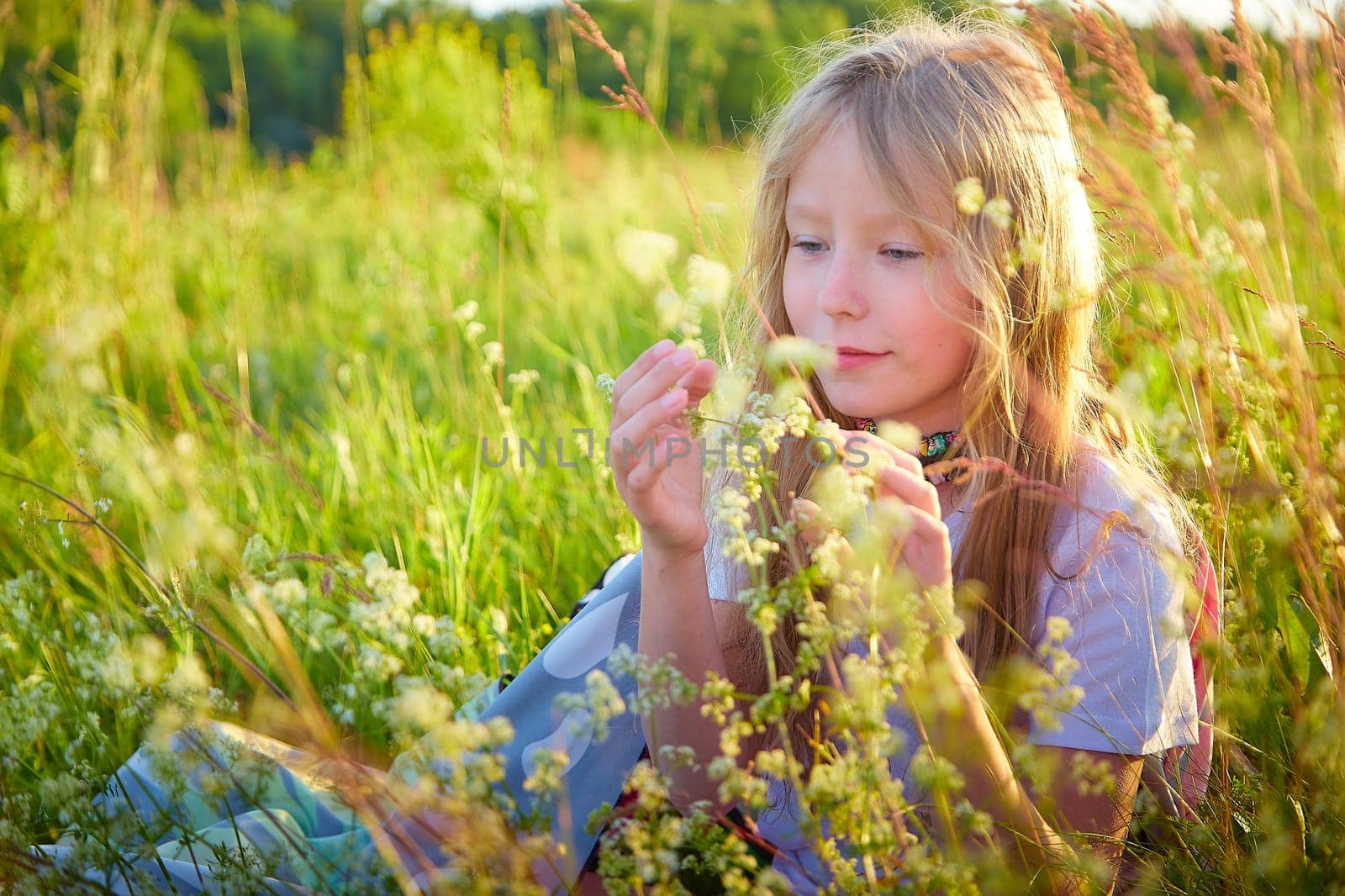 Portrait of pretty blonde girl having fun in a meadow on a natural landscape with grass and flowers on a sunny summer day. Portrait of a teenage child in summer or spring outdoors on field