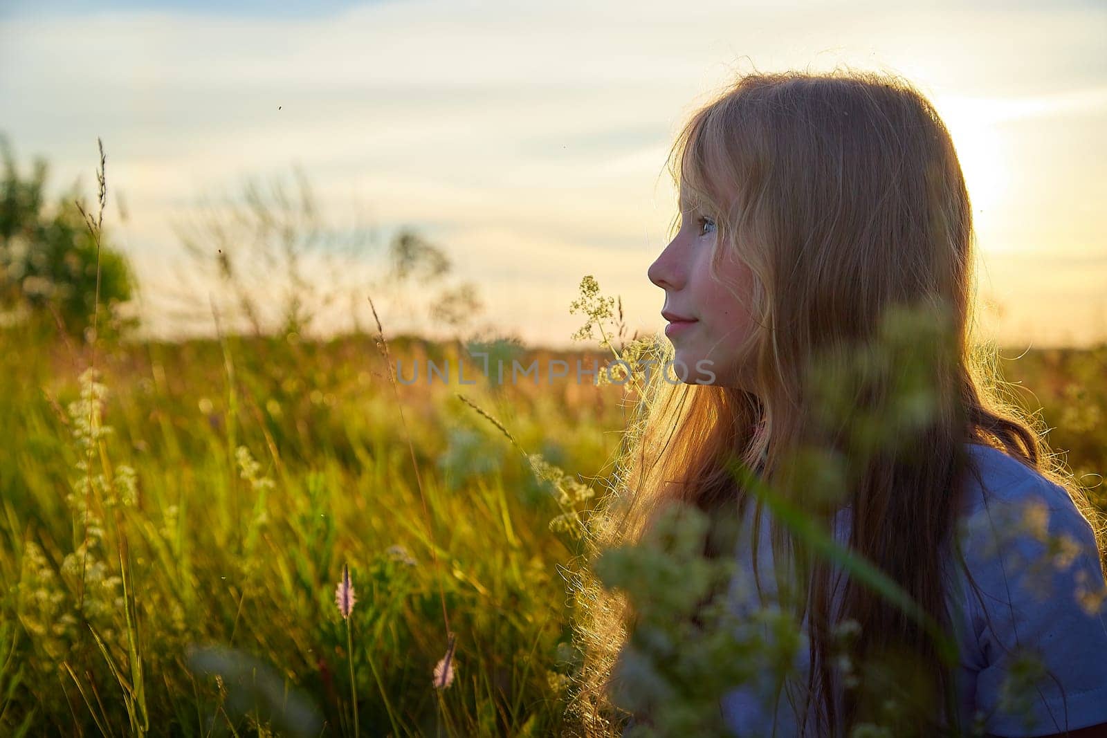 Portrait of pretty blonde girl having fun in a meadow on a natural landscape with grass and flowers on a sunny summer day. Portrait of a teenage child in summer or spring outdoors on field