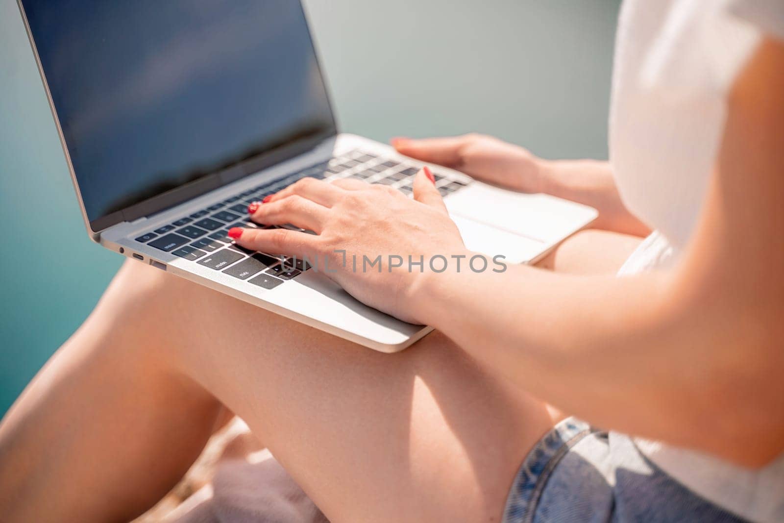 Freelance woman working on a laptop by the sea, typing away on the keyboard while enjoying the beautiful view, highlighting the idea of remote work. by Matiunina