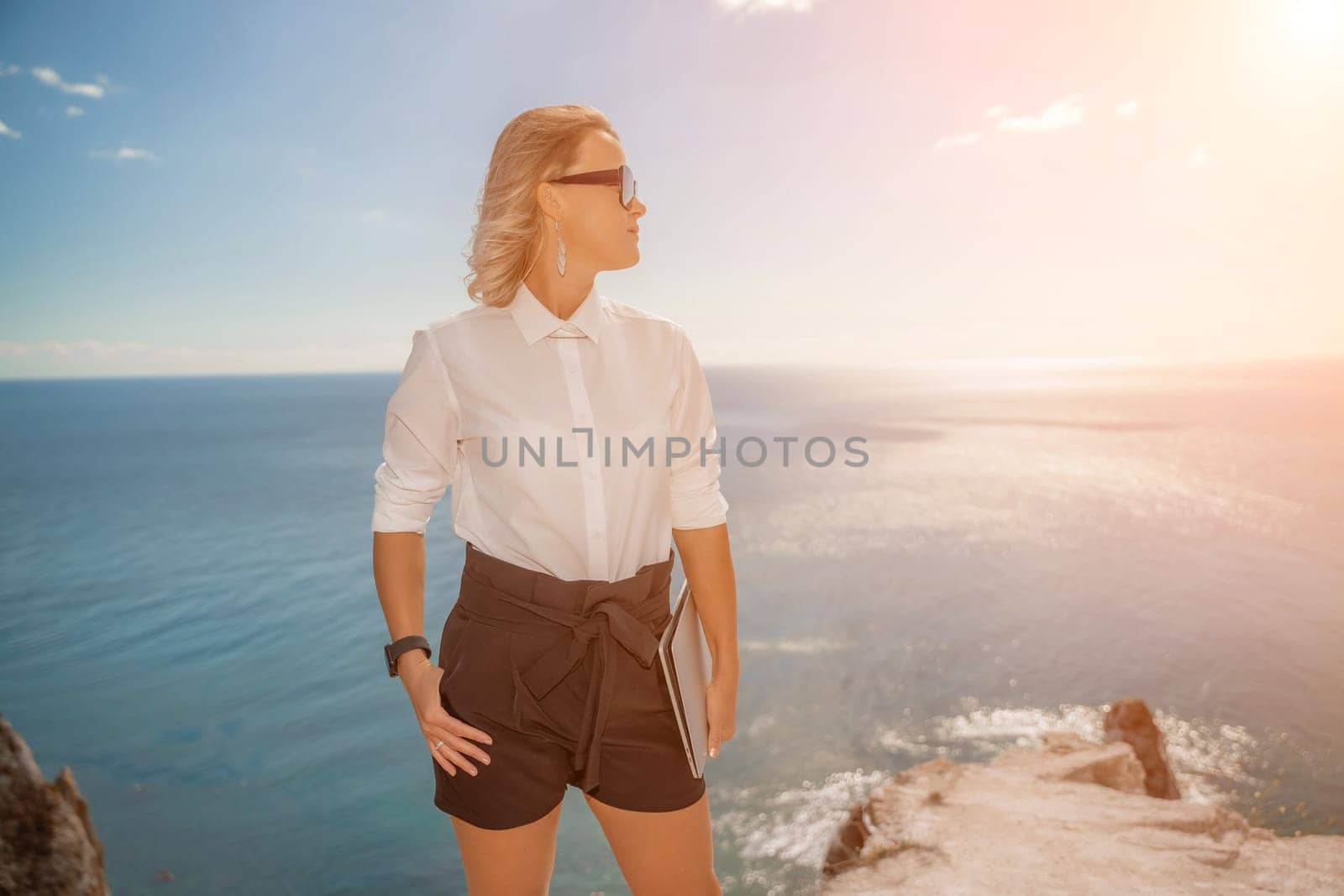 Freelance women sea working on a computer. Pretty middle aged woman with computer and phone outdoors with beautiful sea view. The concept of remote work. by Matiunina