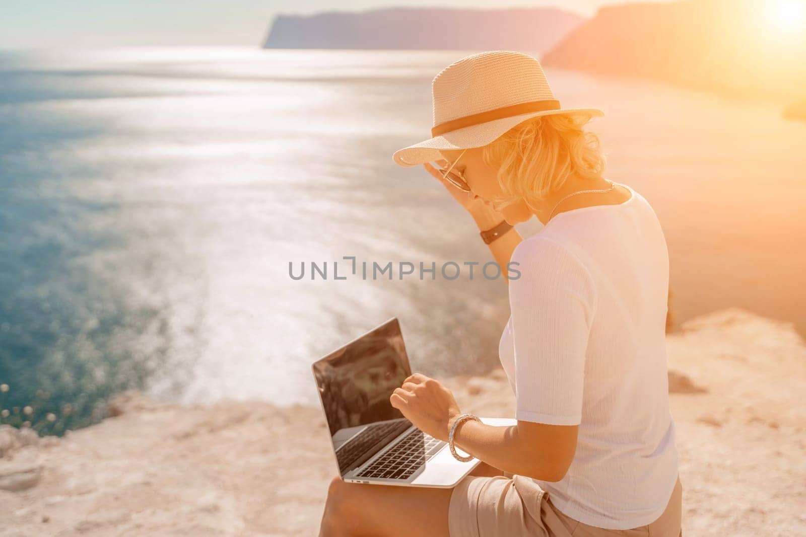 Freelance women sea working on the computer. Good looking middle aged woman typing on a laptop keyboard outdoors with a beautiful sea view. The concept of remote work