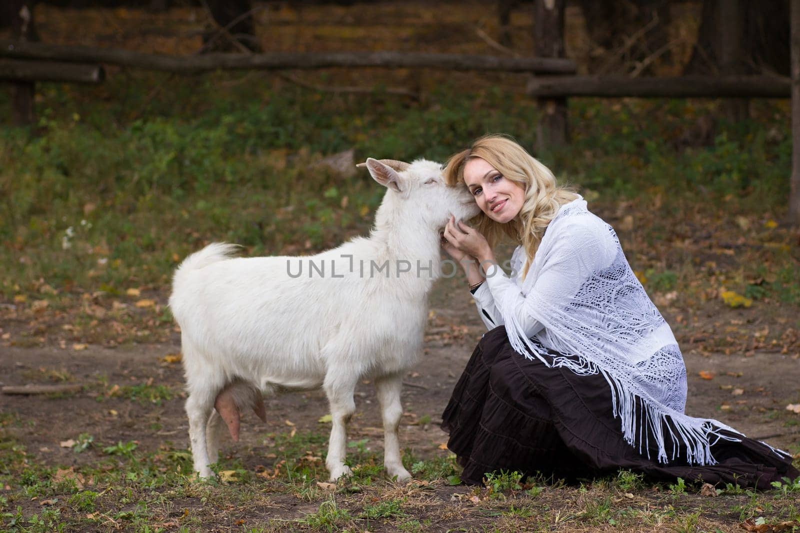 Sweet woman stroking white goats on a green glade