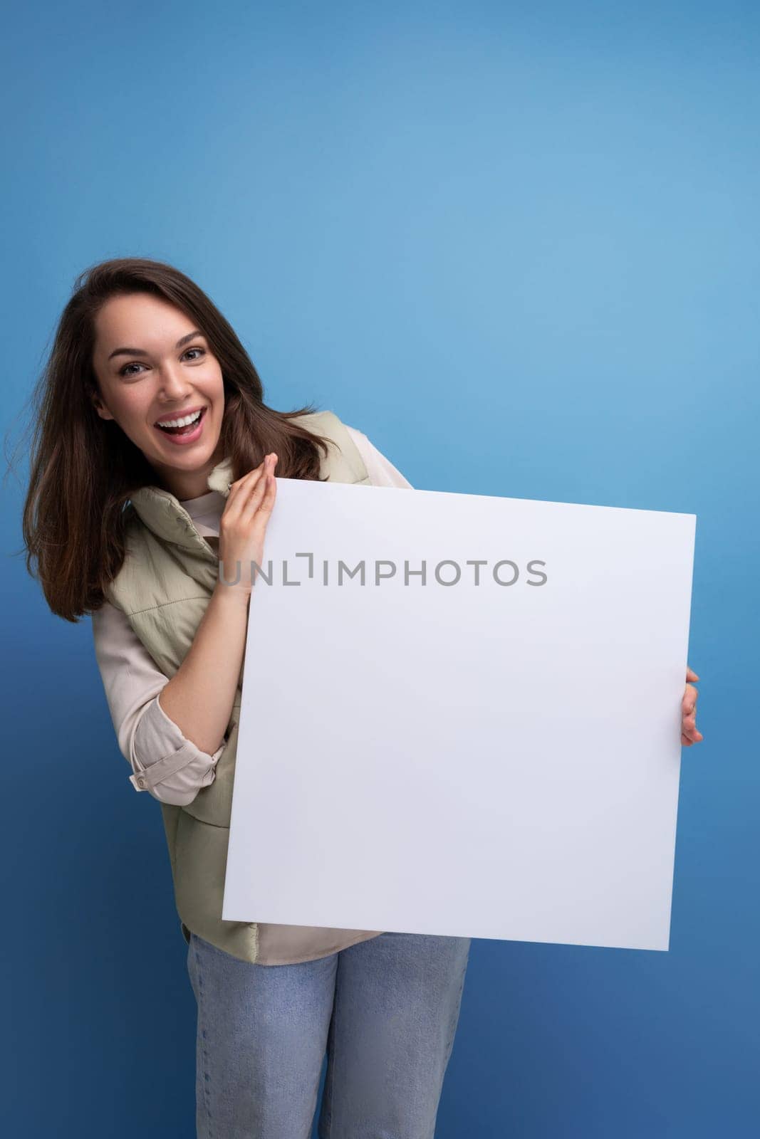 positive young brunette woman showing advertisement on white sheet.