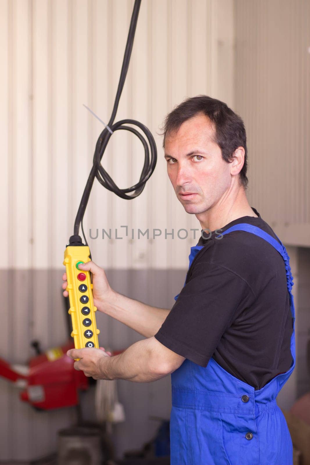 Adult man holding lift control panel in the auto service.