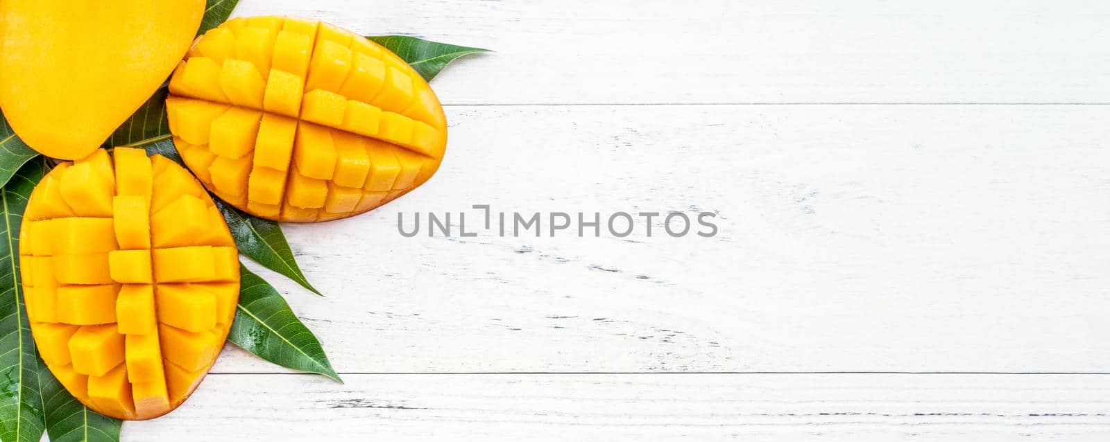 Beautiful chopped mango with green leaves on bright white color timber background. Above Top view, flat lay, copy space, close up. Tropical fruit concept.