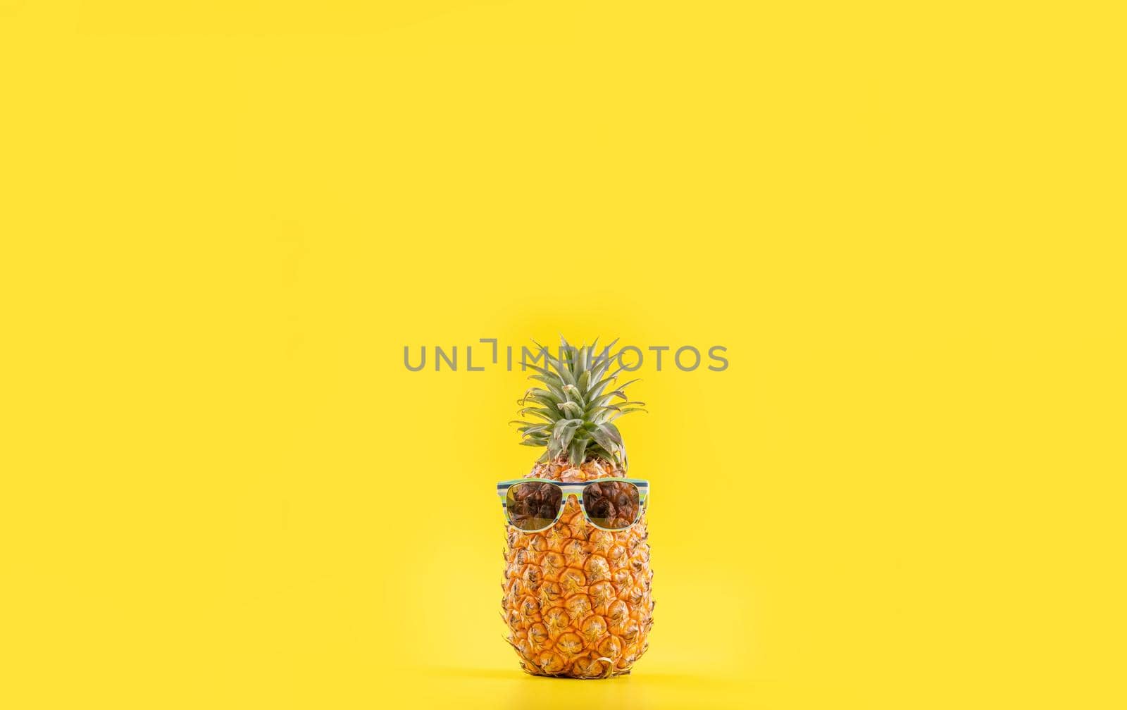 Creative pineapple looking up with sunglasses and shell isolated on yellow background, summer vacation beach idea design pattern, copy space close up by ROMIXIMAGE