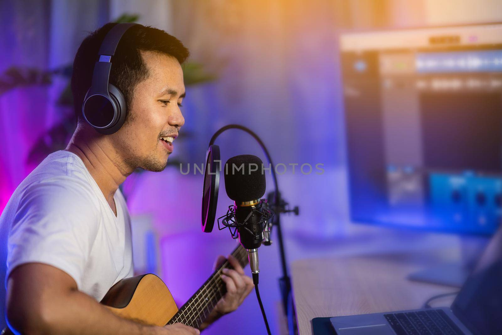 Man singing with headphone and playing guitar recording new song with microphone in the home recording studio by Wmpix