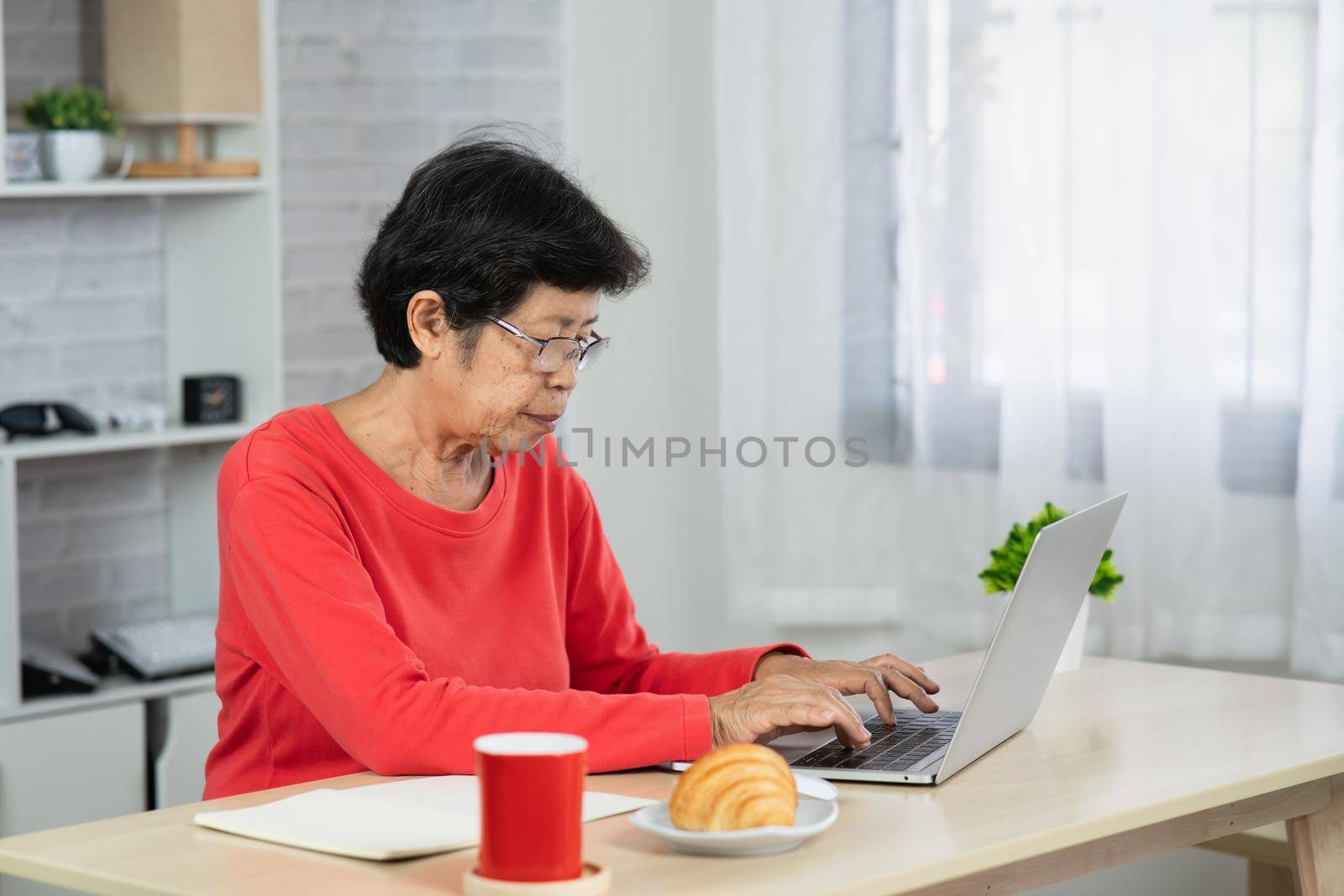 Senior asian woman relaxing using laptop computer while sitting on table. by Wmpix