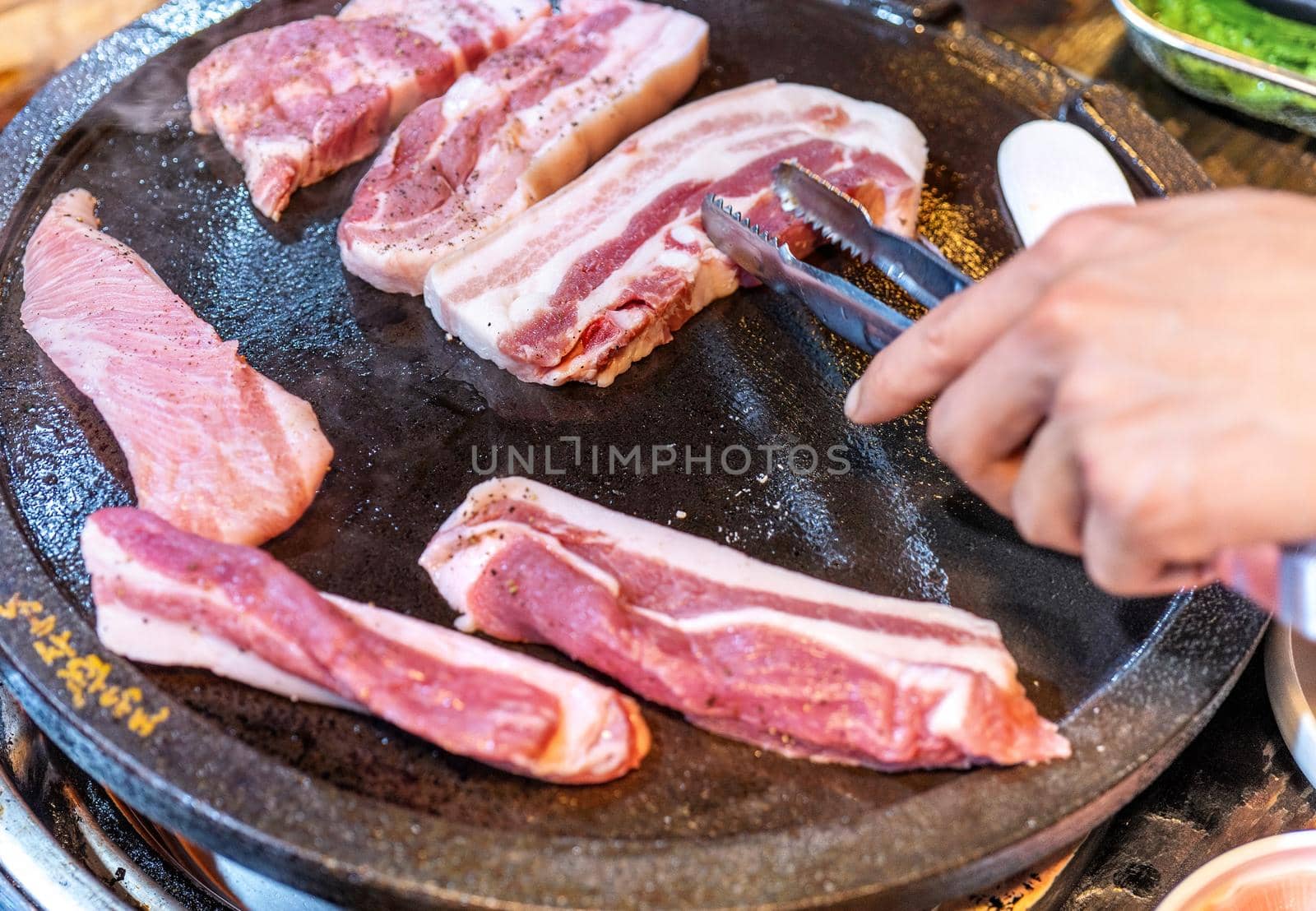 Pan-fried black pork meal in Korea restaurant, fresh delicious korean food cuisine on iron plate with lettuce, close up, copy space, lifestyle